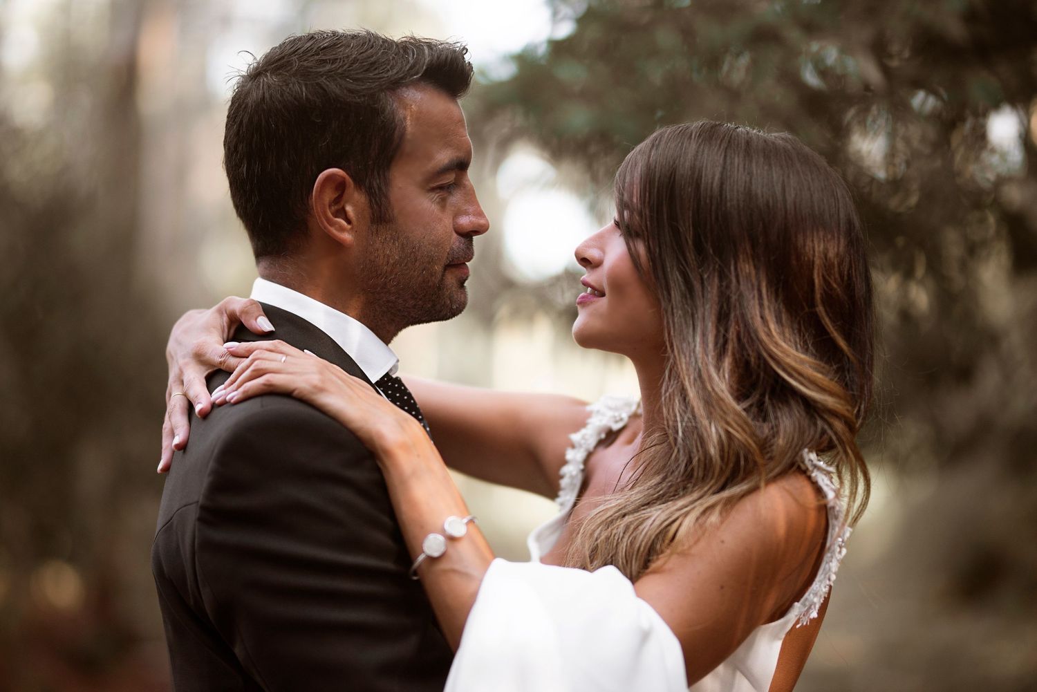 Romantic couple embraces in soft sunlit outdoor setting during wedding photoshoot.