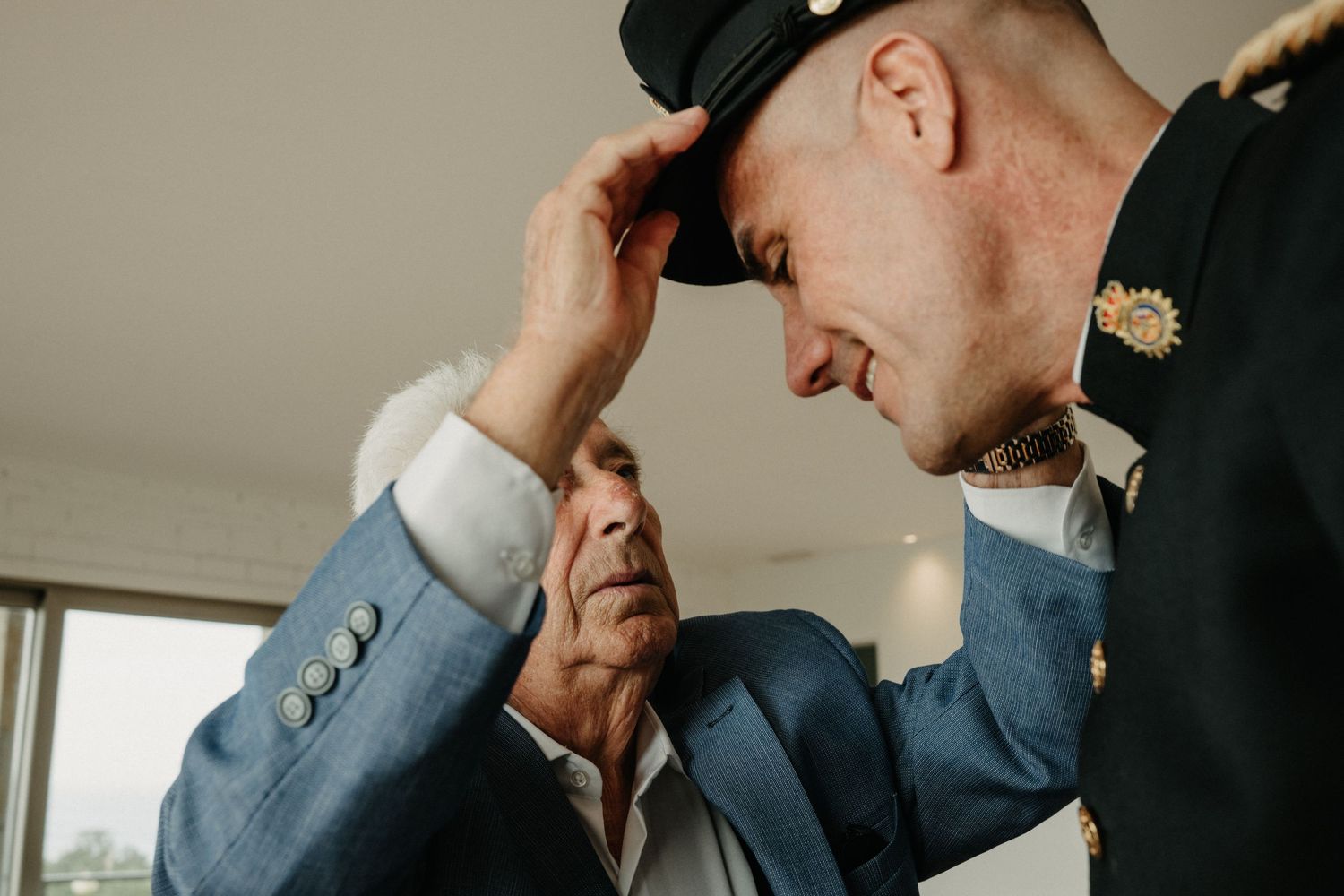 A groom adjusts his tie while getting ready for a wedding ceremony in a light-filled room.