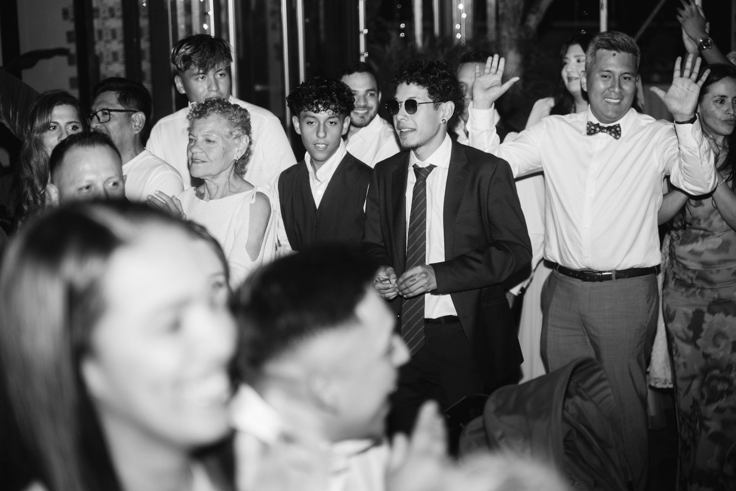 Black and white photo of wedding guests dancing and celebrating on a crowded dance floor.