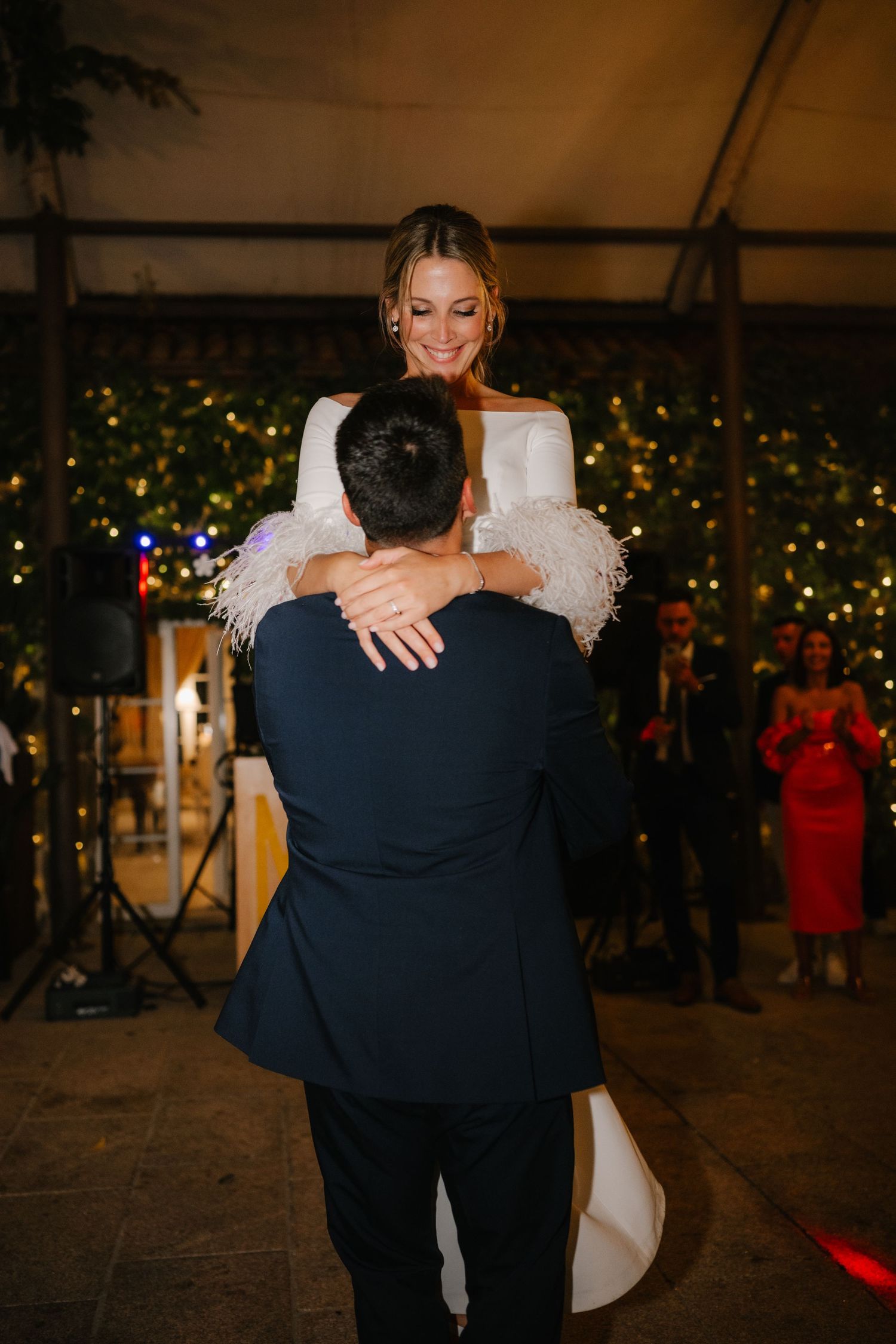A couple embraces on the dance floor at a wedding reception with twinkling Christmas lights in the background.