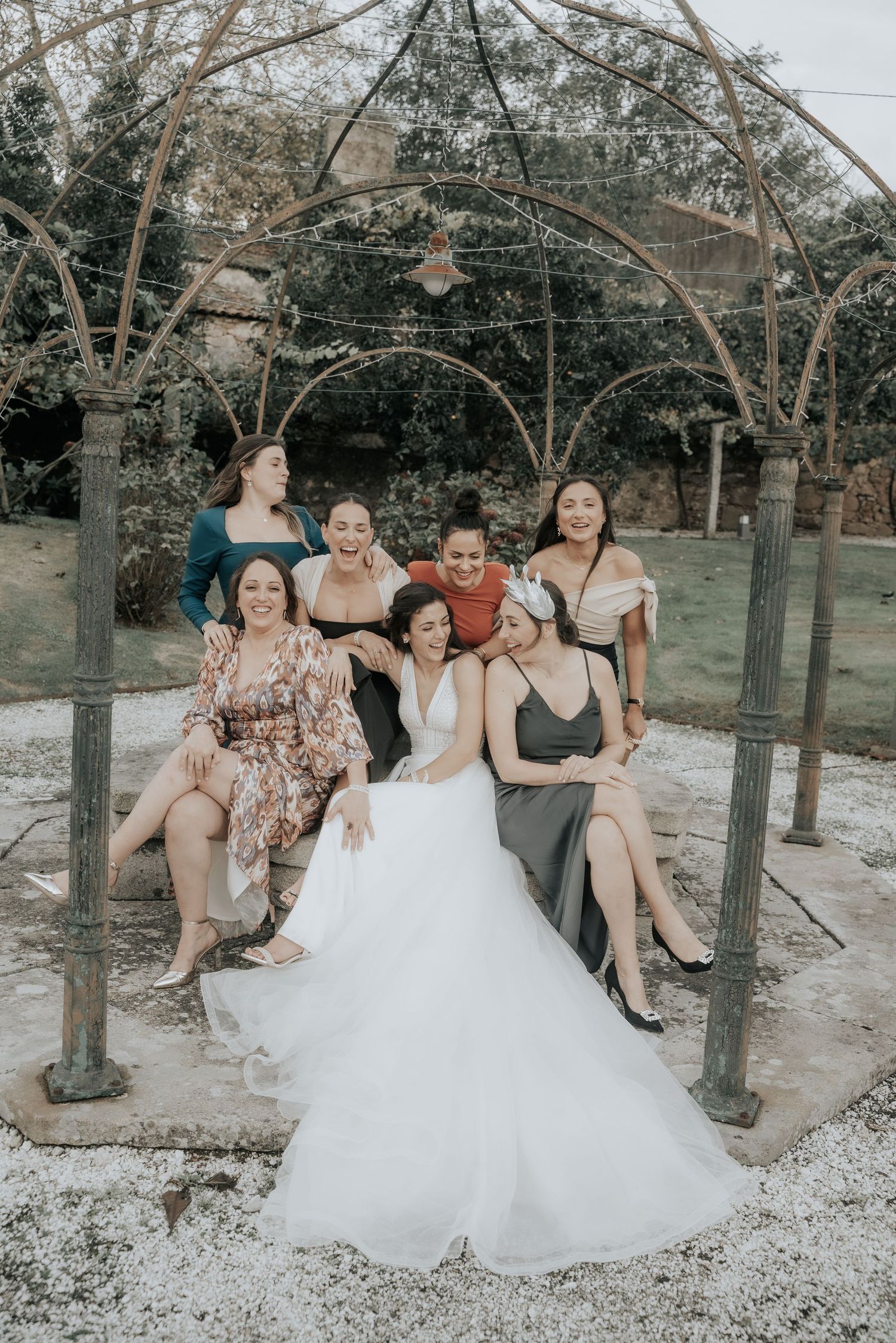A group of friends in formal attire sit together on a swing set in an outdoor garden setting.
