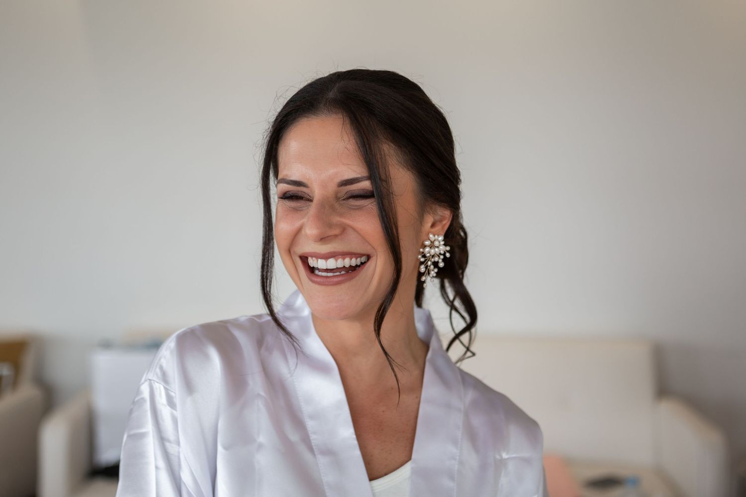 Bride wearing a white button-up shirt smiles joyfully while getting ready for her wedding day.