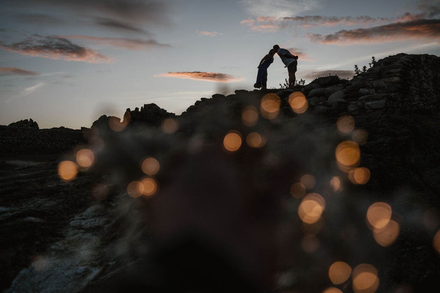 Dramatic sunset sky with silhouetted mountains and glowing bokeh lights creates a moody atmospheric landscape scene.