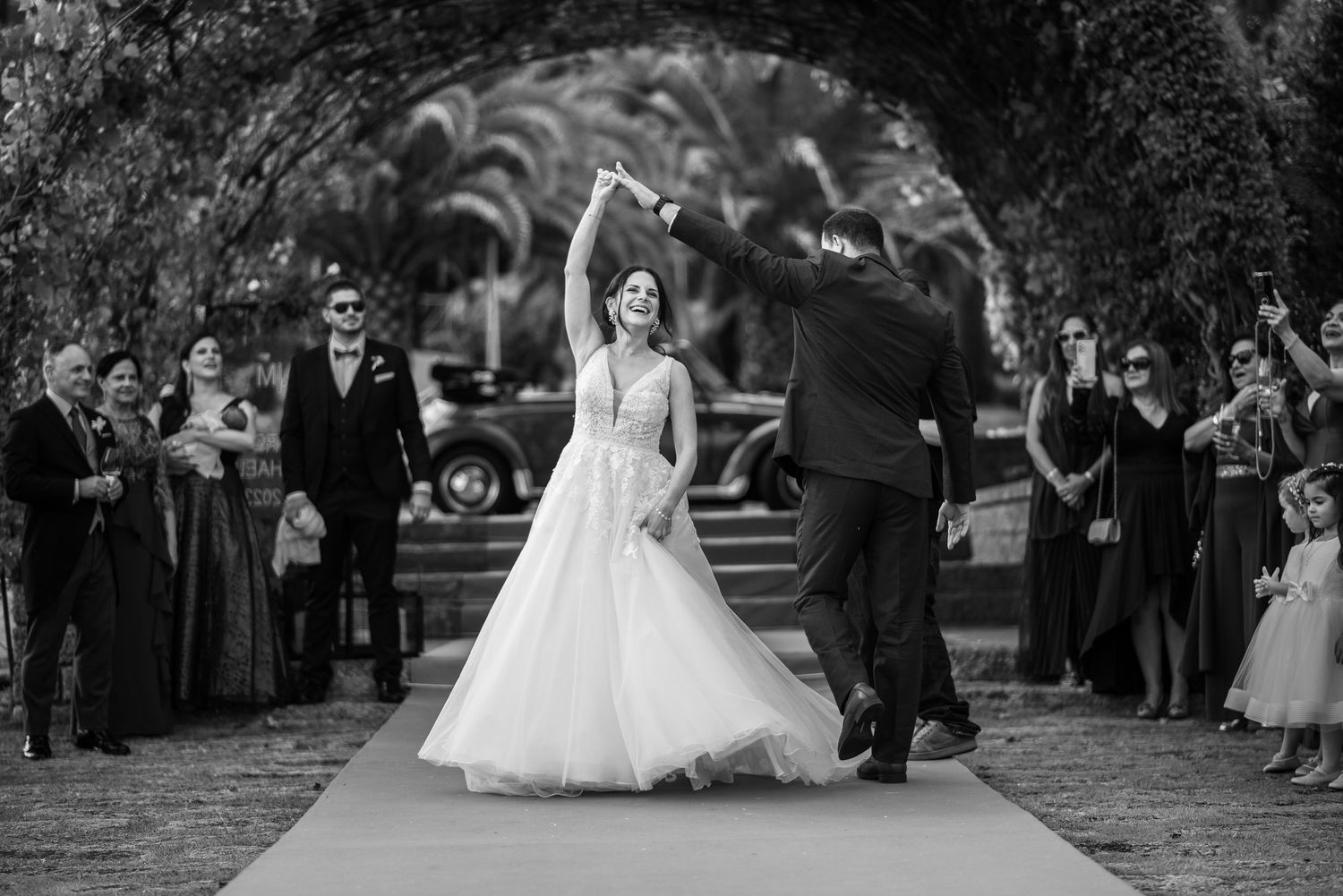 A black and white wedding photo captures a couple dancing surrounded by guests at an outdoor reception.