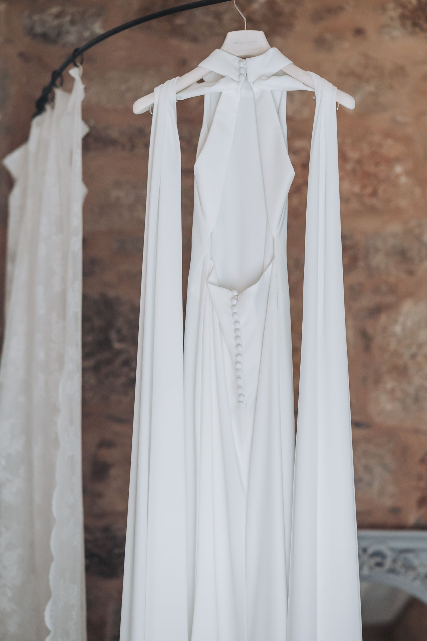 White wedding dresses hanging on hangers against a rustic brick wall background.