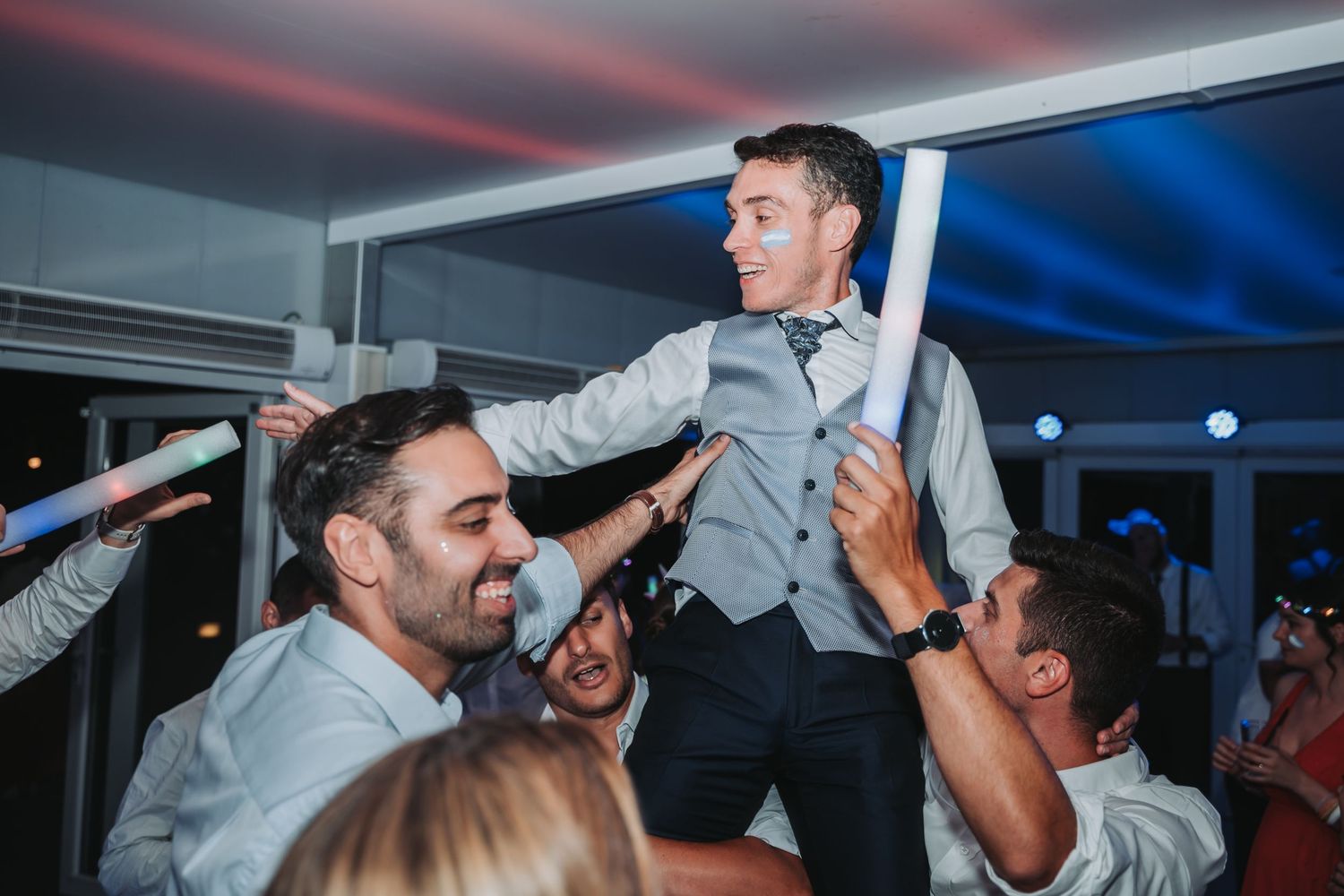 People dancing and celebrating at a wedding reception with colorful lighting and energetic atmosphere.