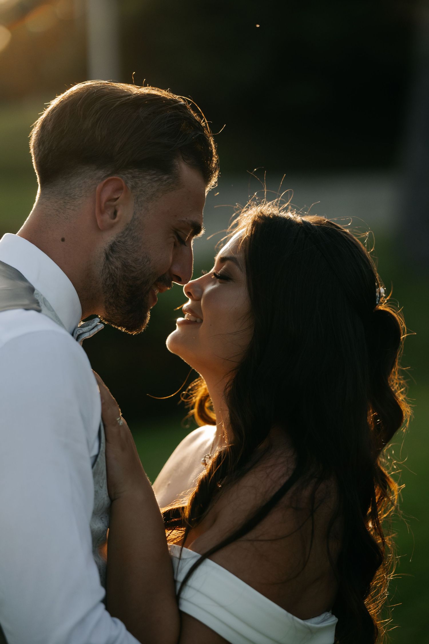 Romantic couple embraces in golden sunlight creating silhouettes against warm backlit glow at sunset.