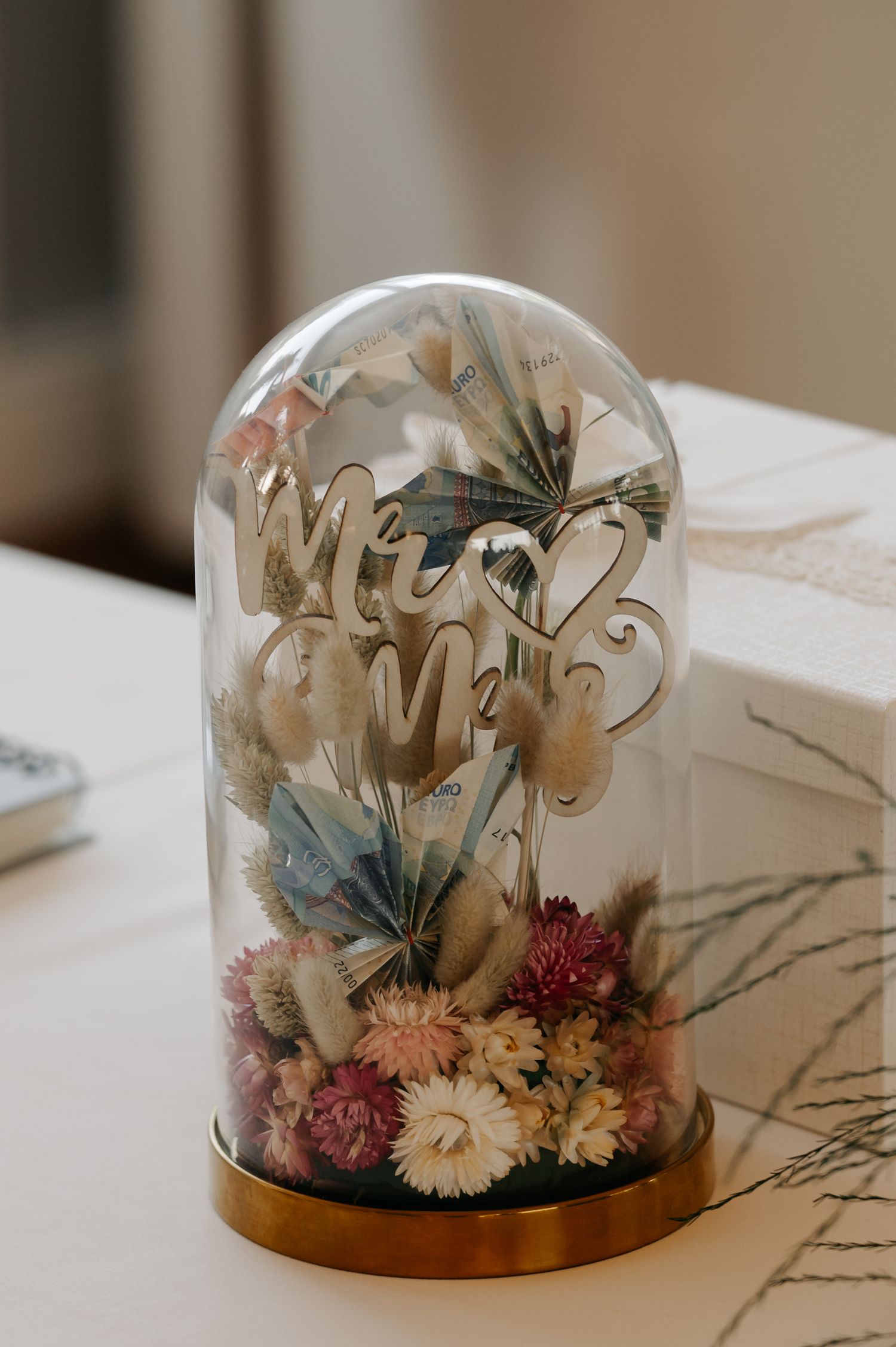 A glass dome display featuring preserved dried flowers in soft beige and pink tones with delicate branches.