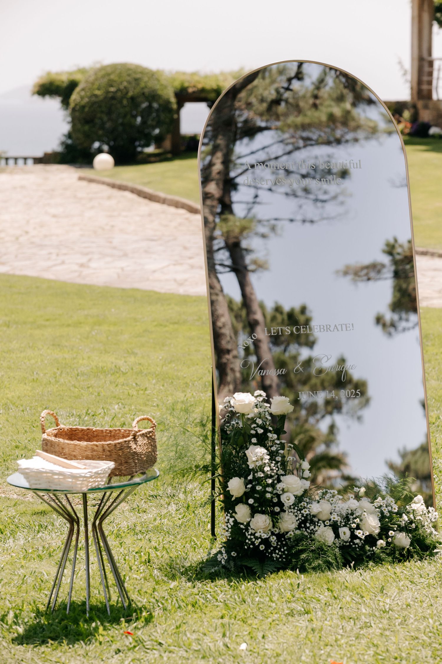 A decorative mirror and chair setup on green grass creates an elegant outdoor wedding vignette.