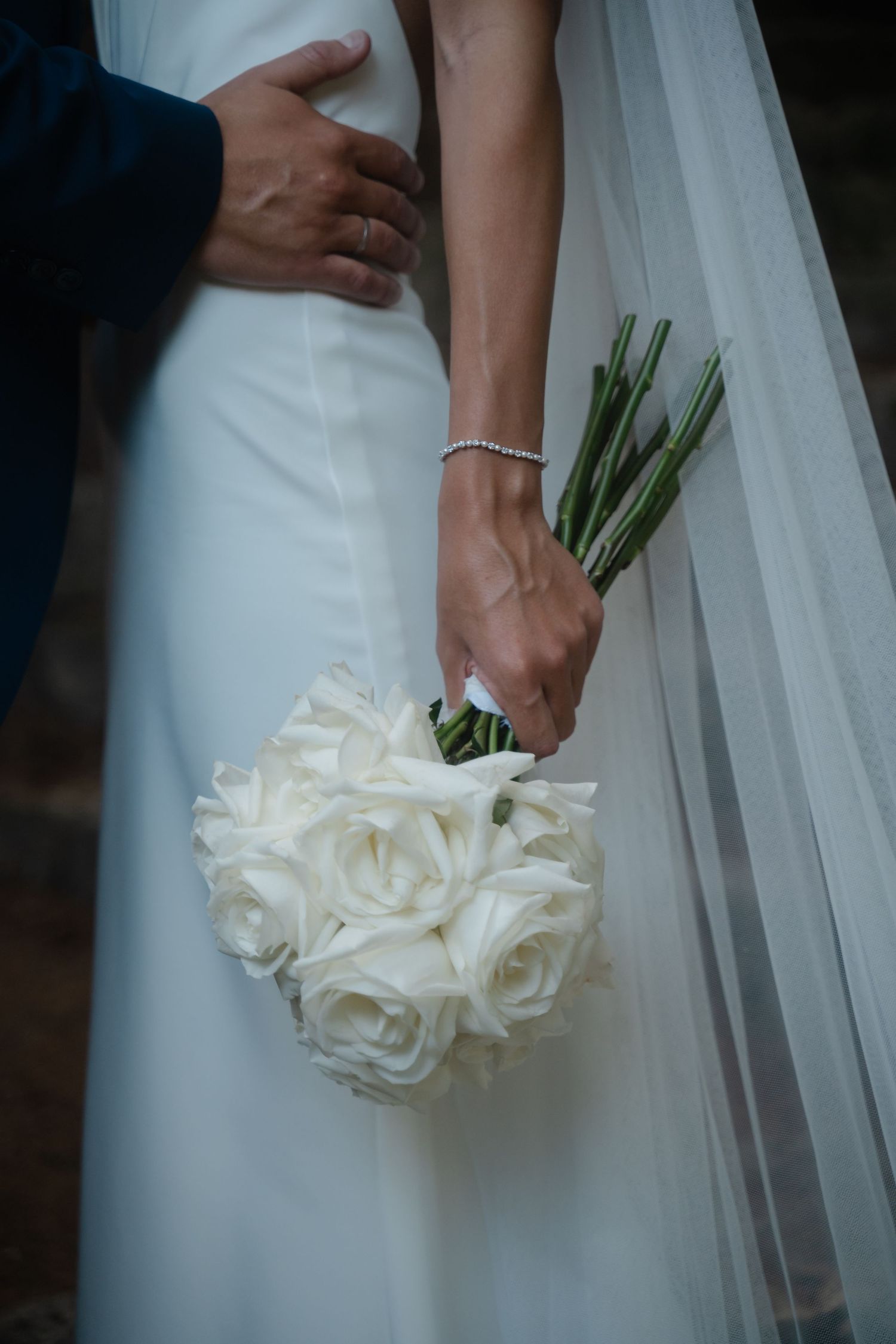 Close-up shots of a bride holding an elegant white rose bouquet against her wedding dress.