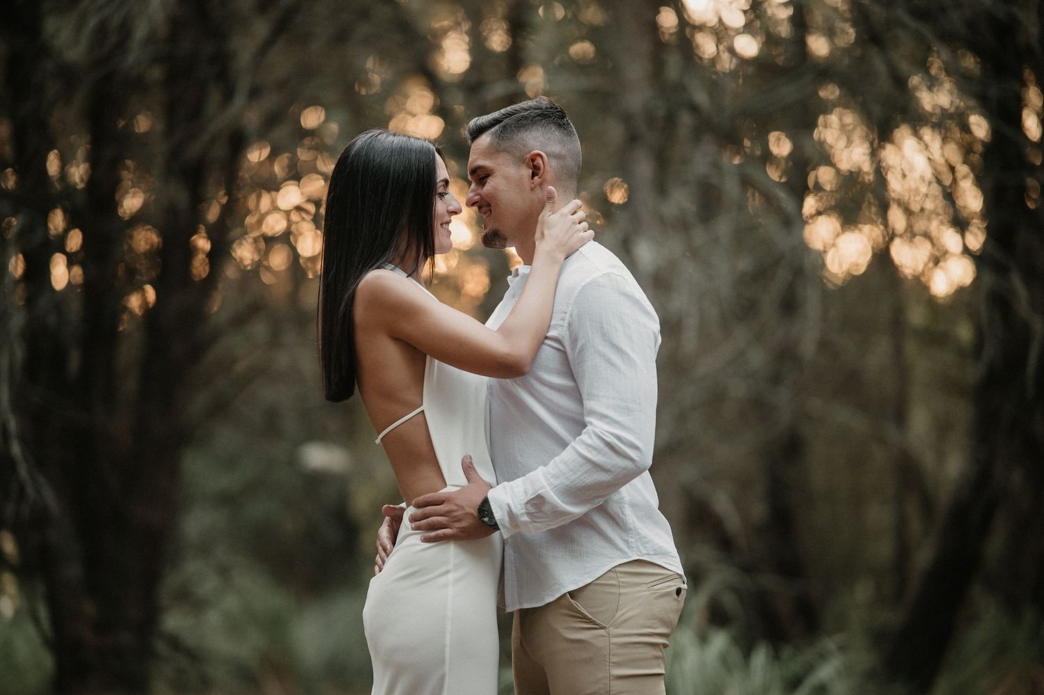 Couple in wedding attire shares romantic moments in a wooded area during sunset, creating an intimate atmosphere.