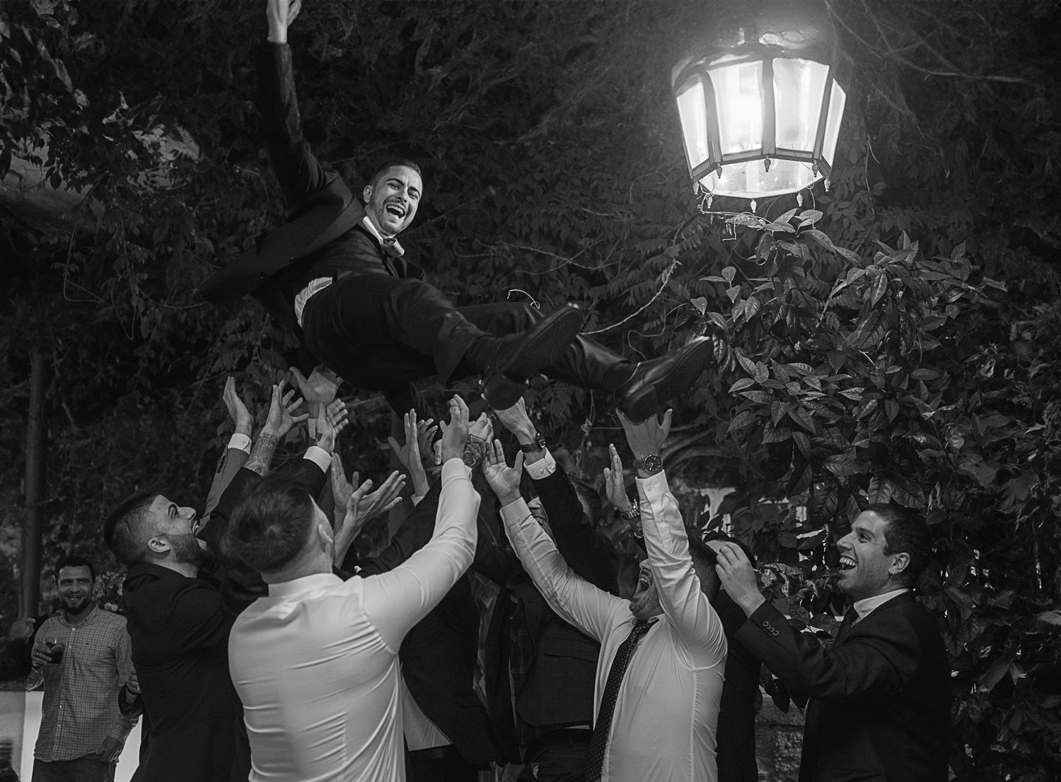 A black and white photo of a couple dancing together under an illuminated garden lantern at night.
