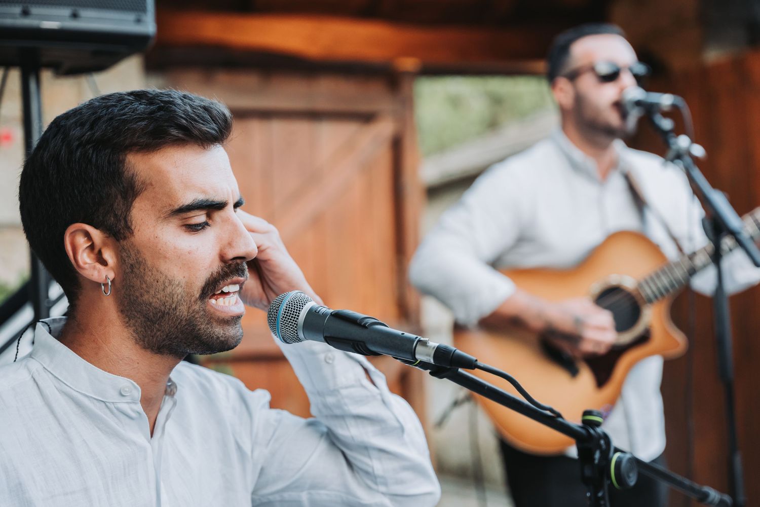 Musicians perform live at a rustic venue with acoustic guitars and microphones.