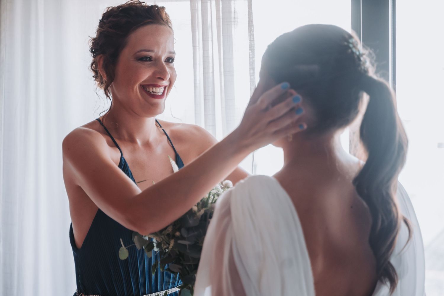 A group of women in formal attire laugh and smile together while getting ready for a special event.