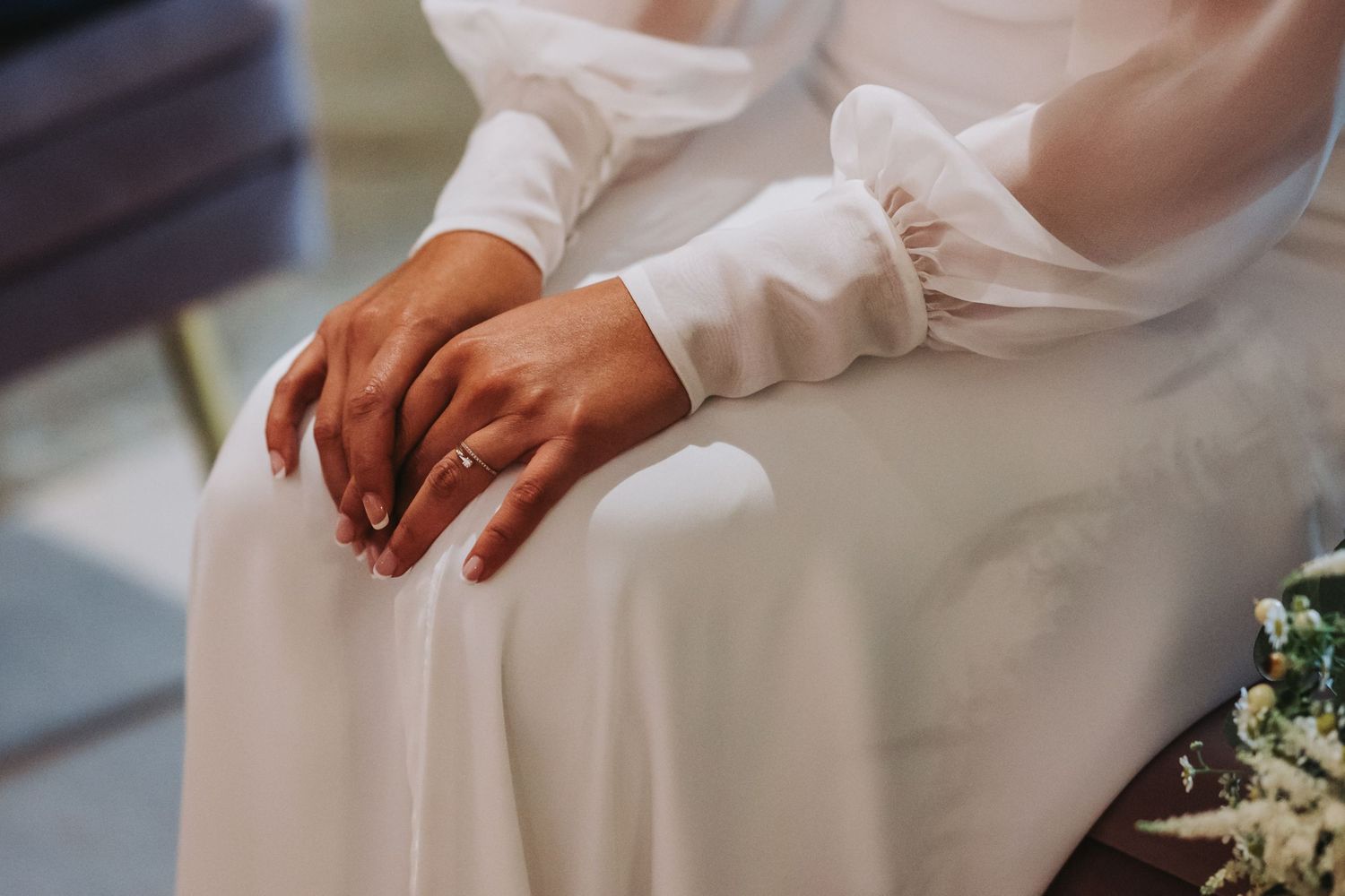 Hands rest gently on white fabric with delicate white flowers in soft lighting.