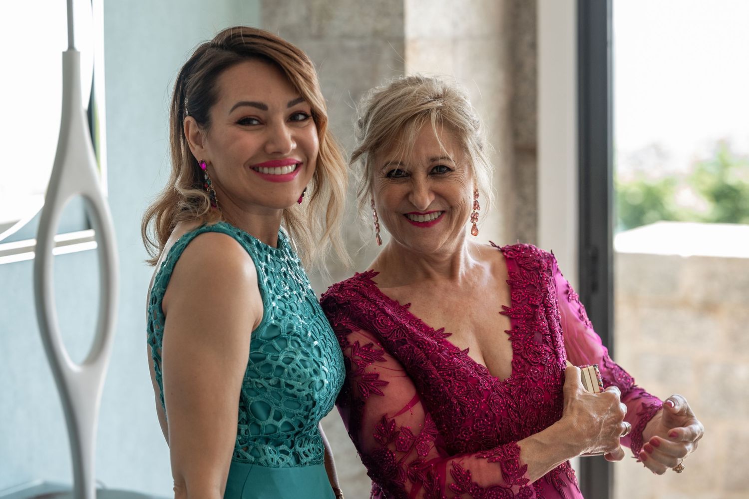Wedding party members in teal and burgundy dresses smile and laugh together during a photo session.