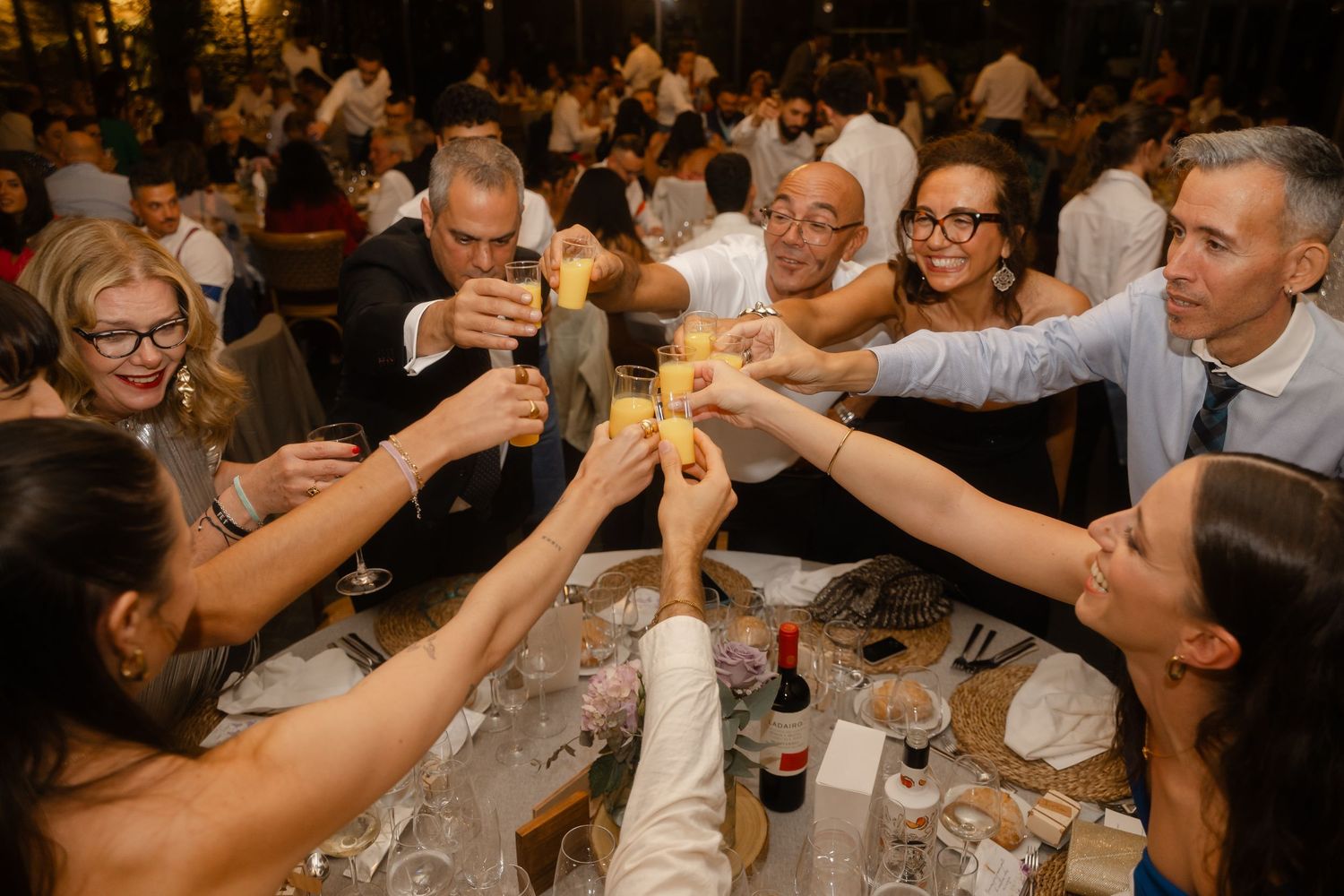 A group of people raise their glasses in a celebratory toast at a crowded dinner event.