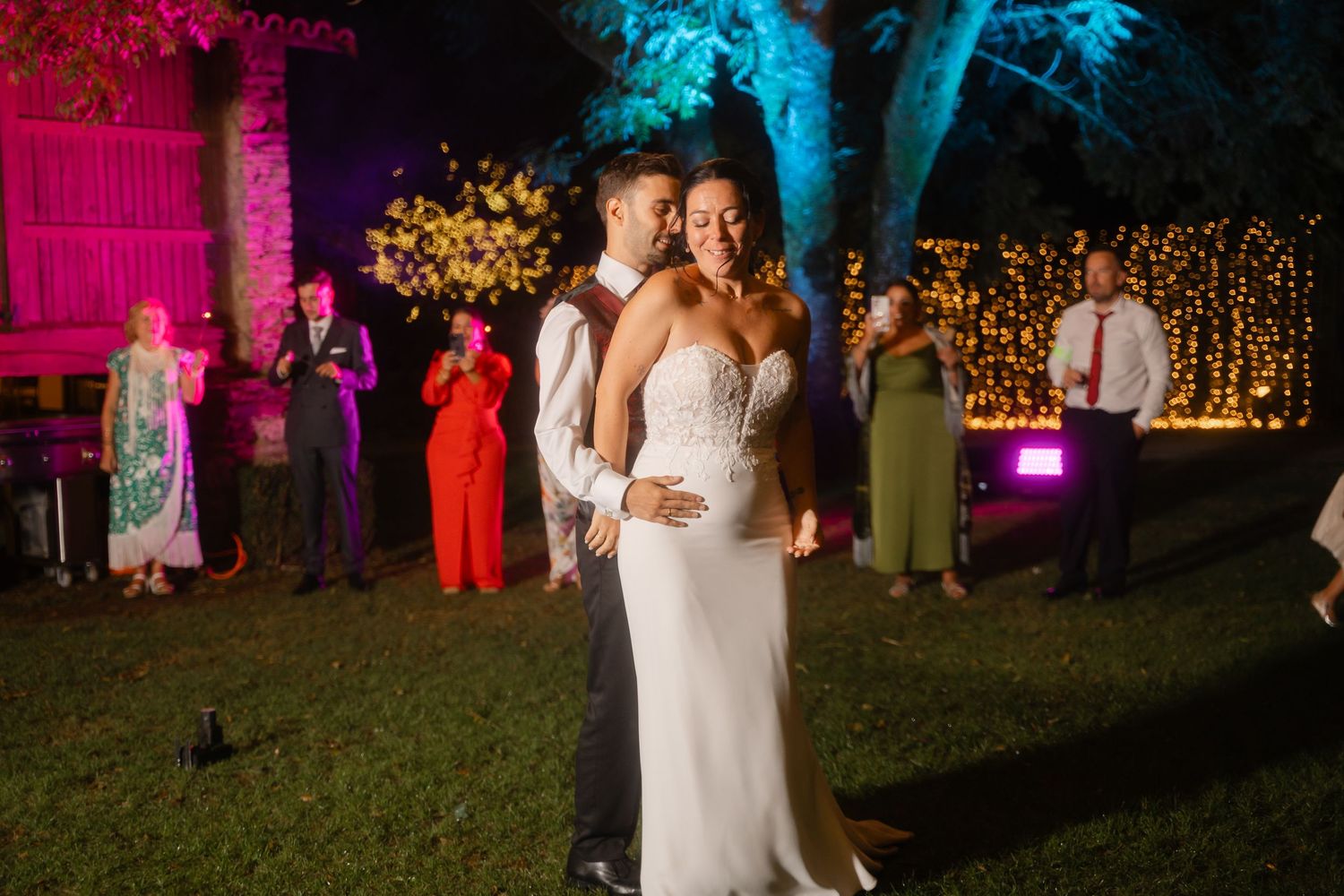 Wedding celebration at night with string lights and pink uplighting creating a romantic outdoor atmosphere.