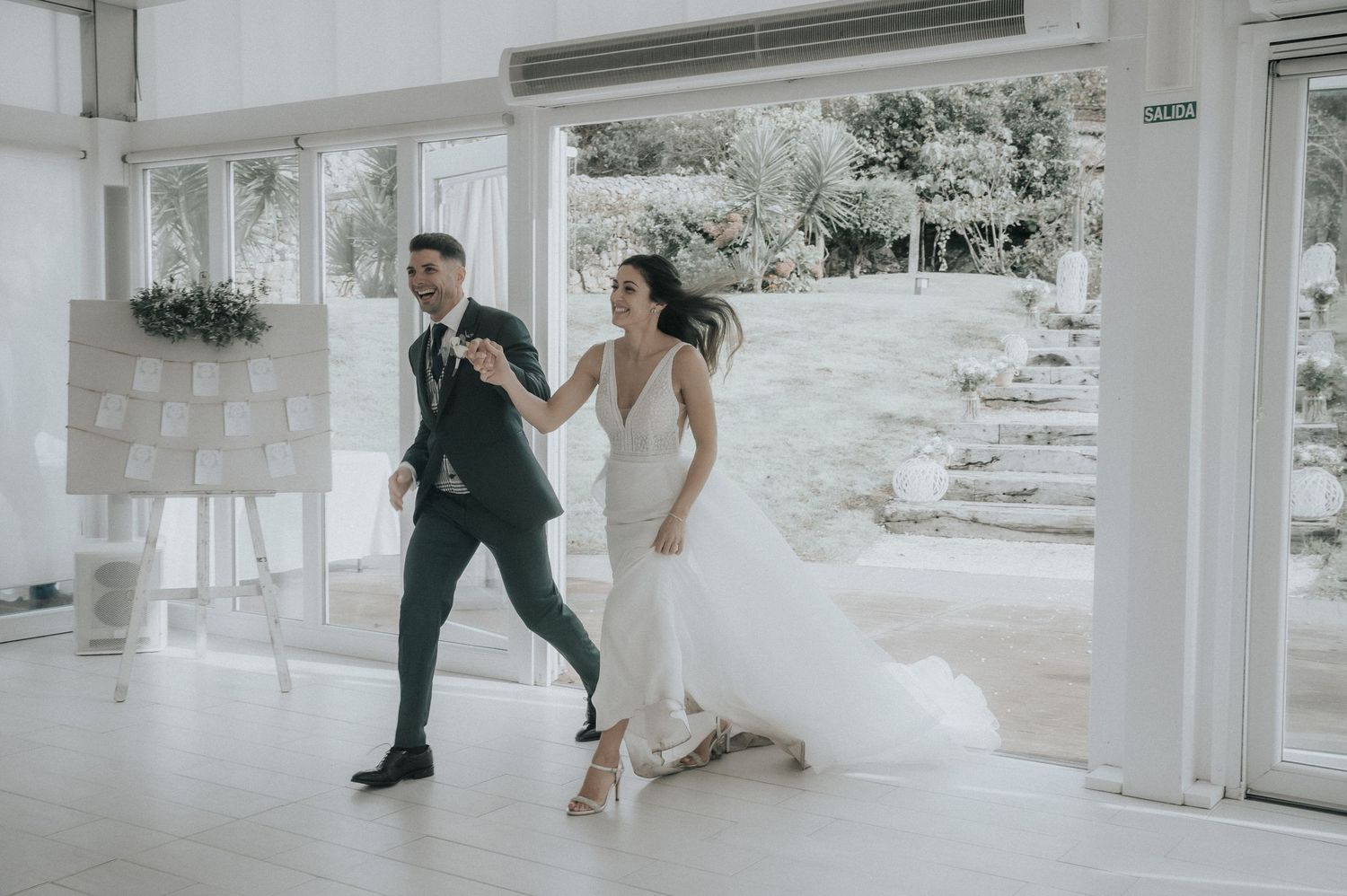 A couple shares a joyful dance moment in an elegant white venue during their wedding celebration.