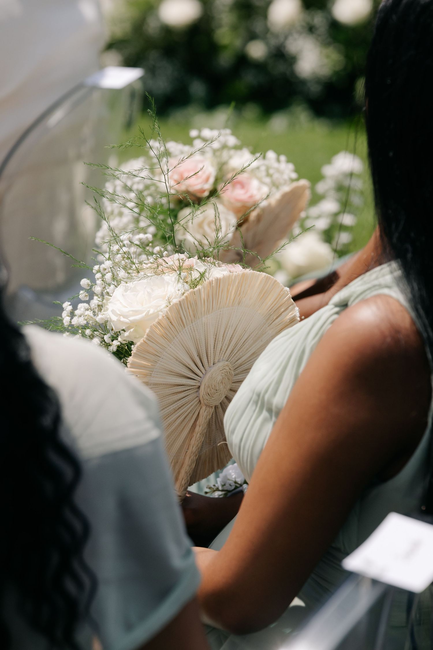 A delicate hand-held fan adorned with baby's breath flowers and soft pink roses creates an elegant wedding accessory detail.