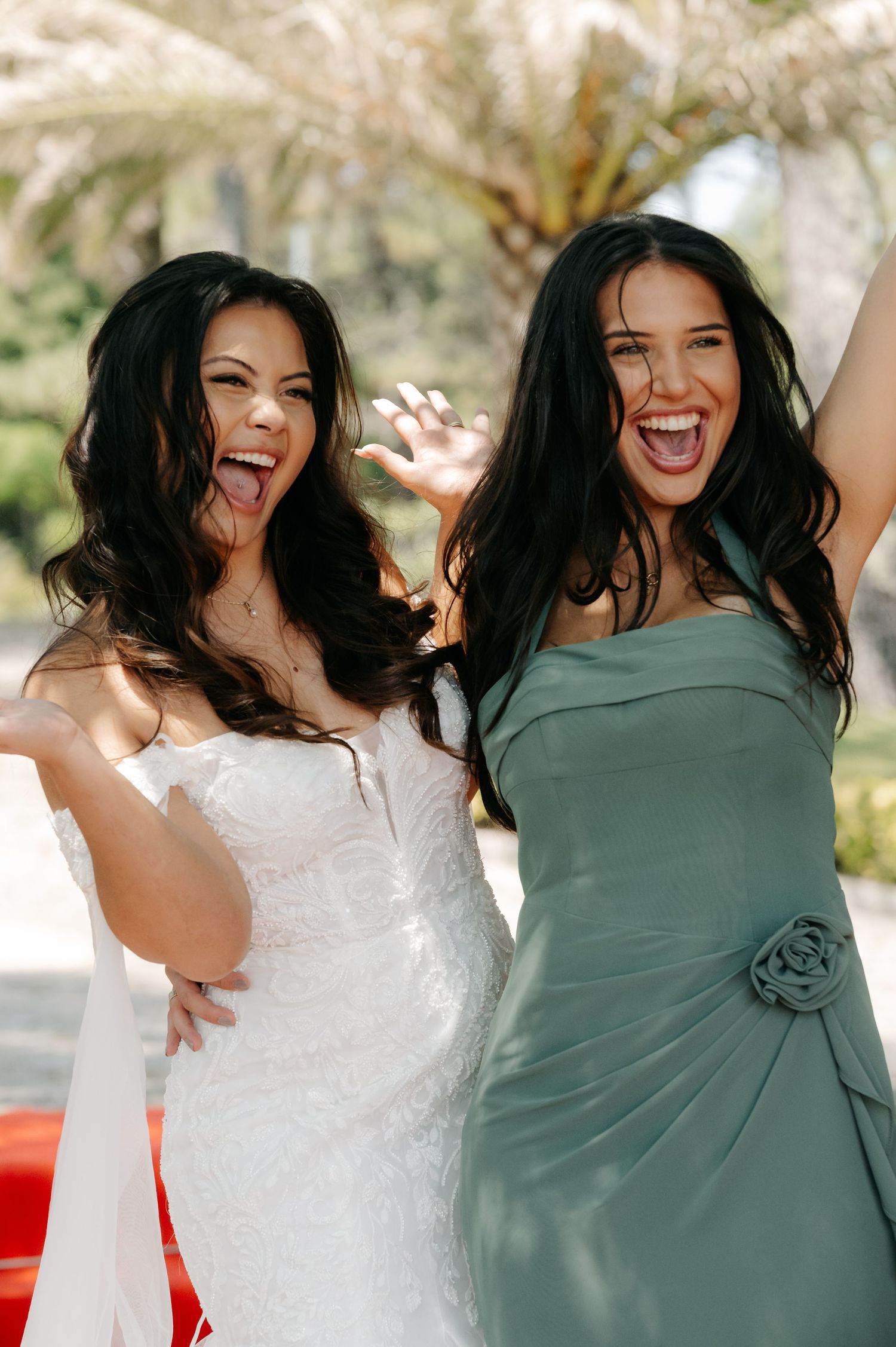 Two friends in white and sage green dresses share joyful laughter during an outdoor photo session.