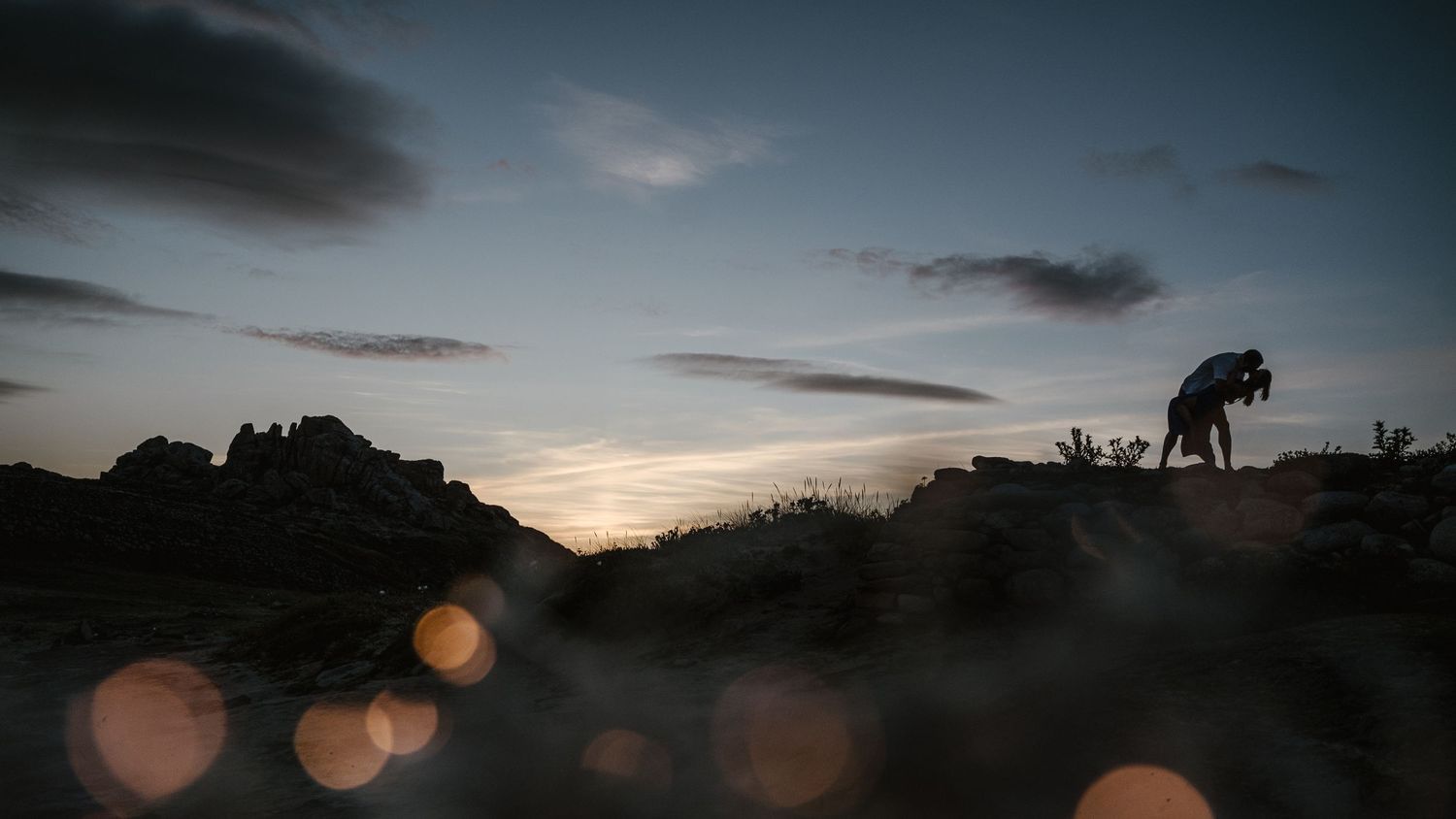 A panoramic view of a dramatic sunset over a desert landscape with silhouetted mountains and glowing orange sky.