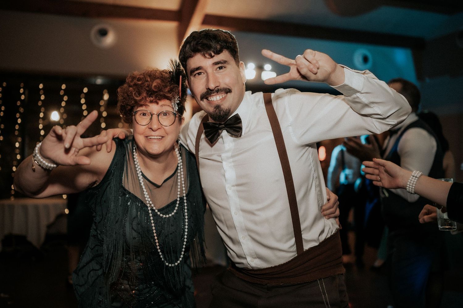 Party guests pose and dance energetically at a dimly lit reception with string lights.
