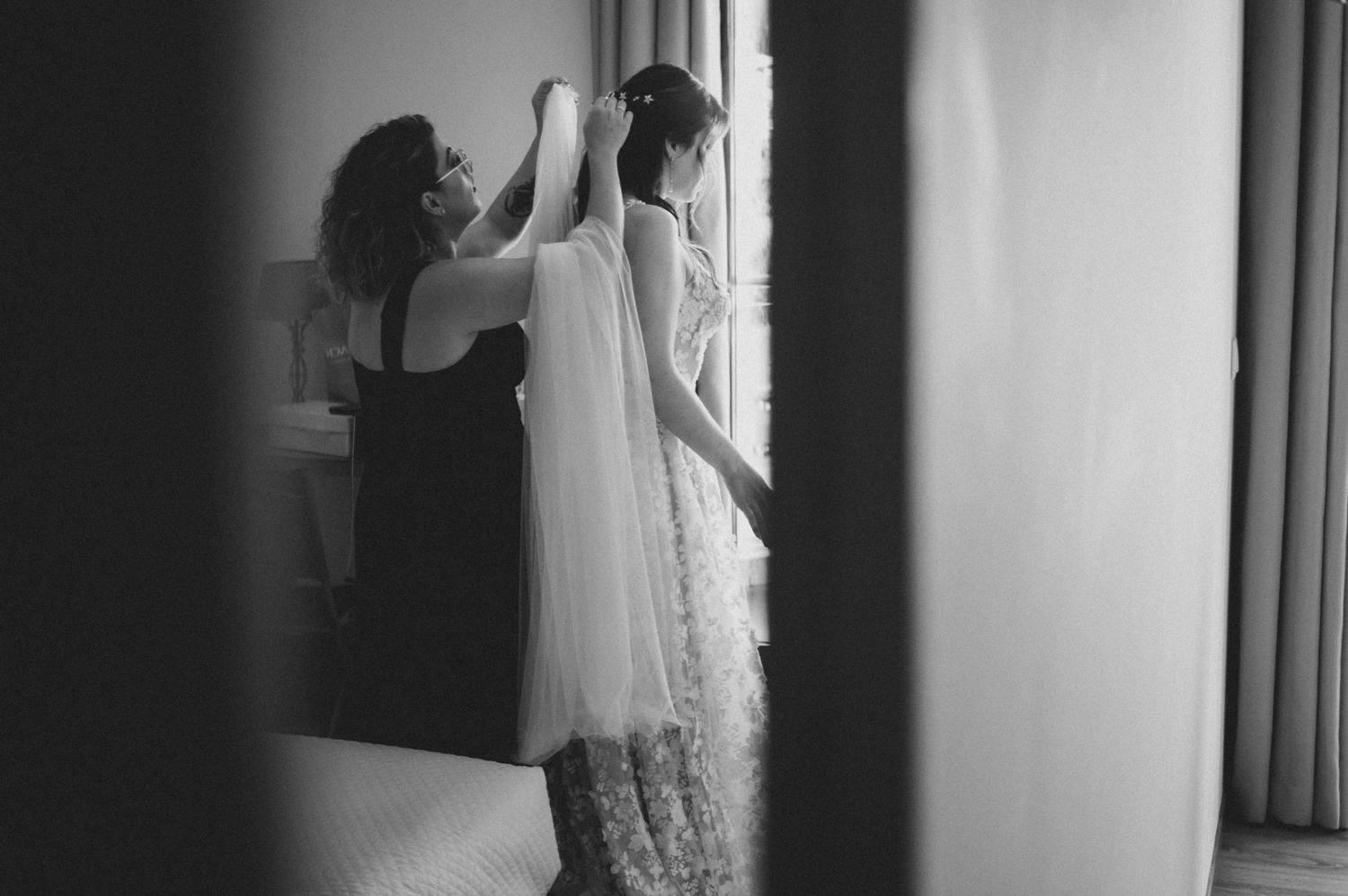 A bride in a white wedding dress stands in front of a window creating a dramatic silhouette effect.