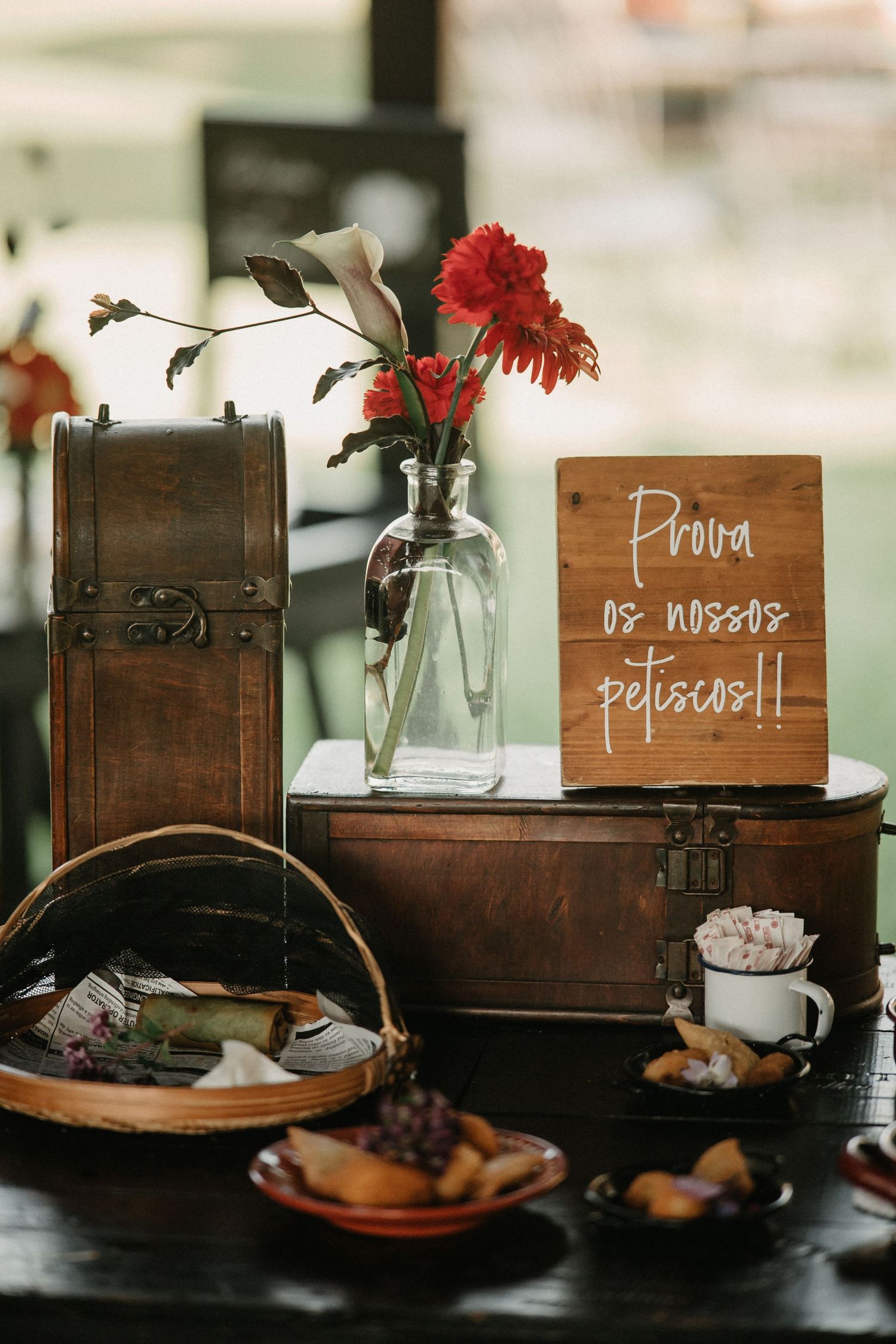 Rustic wooden table settings with red carnations in glass vases and handwritten signs for a wedding reception.