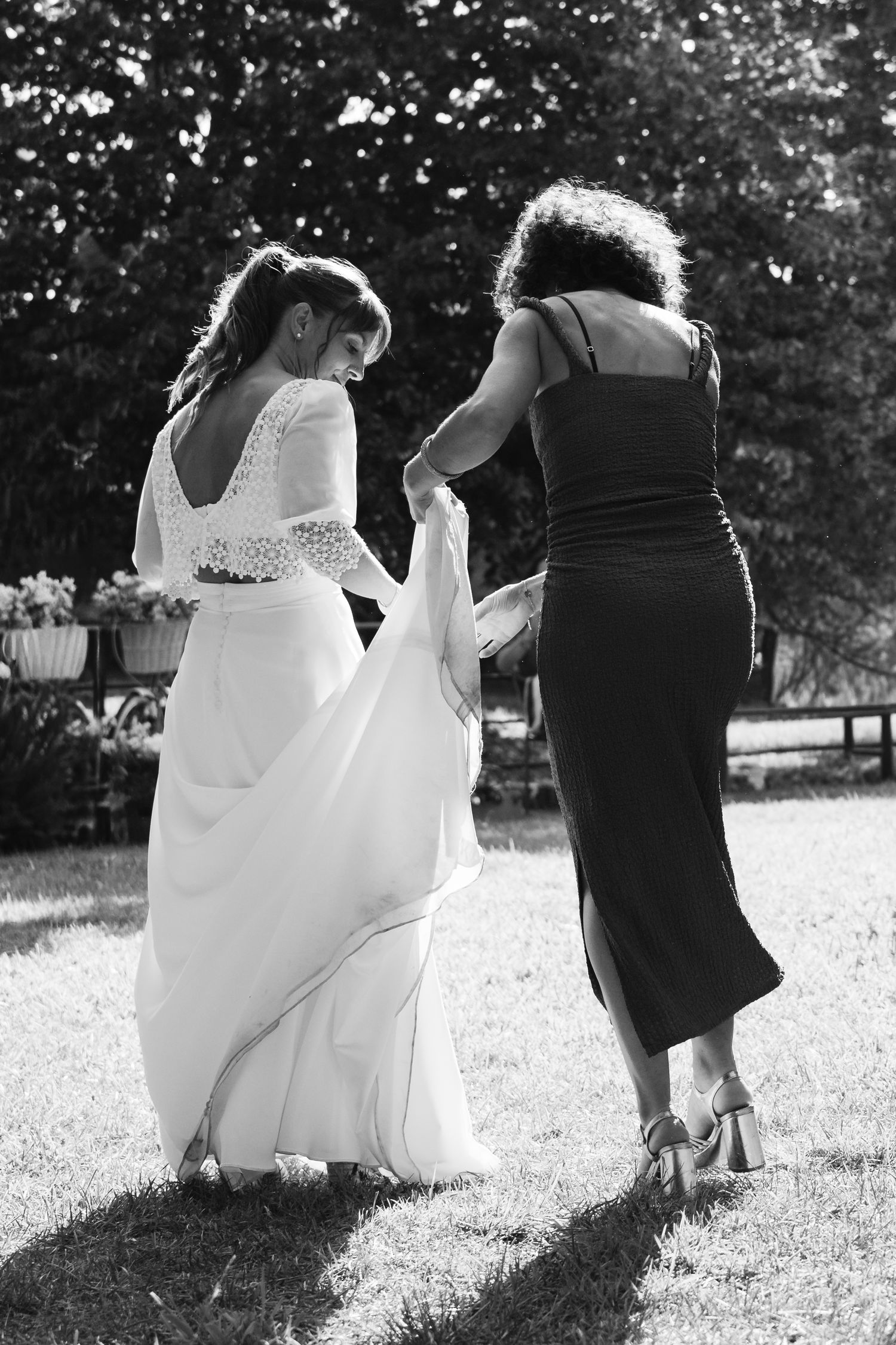 Black and white silhouettes of bridesmaids in dresses walking across a grassy field at a wedding.