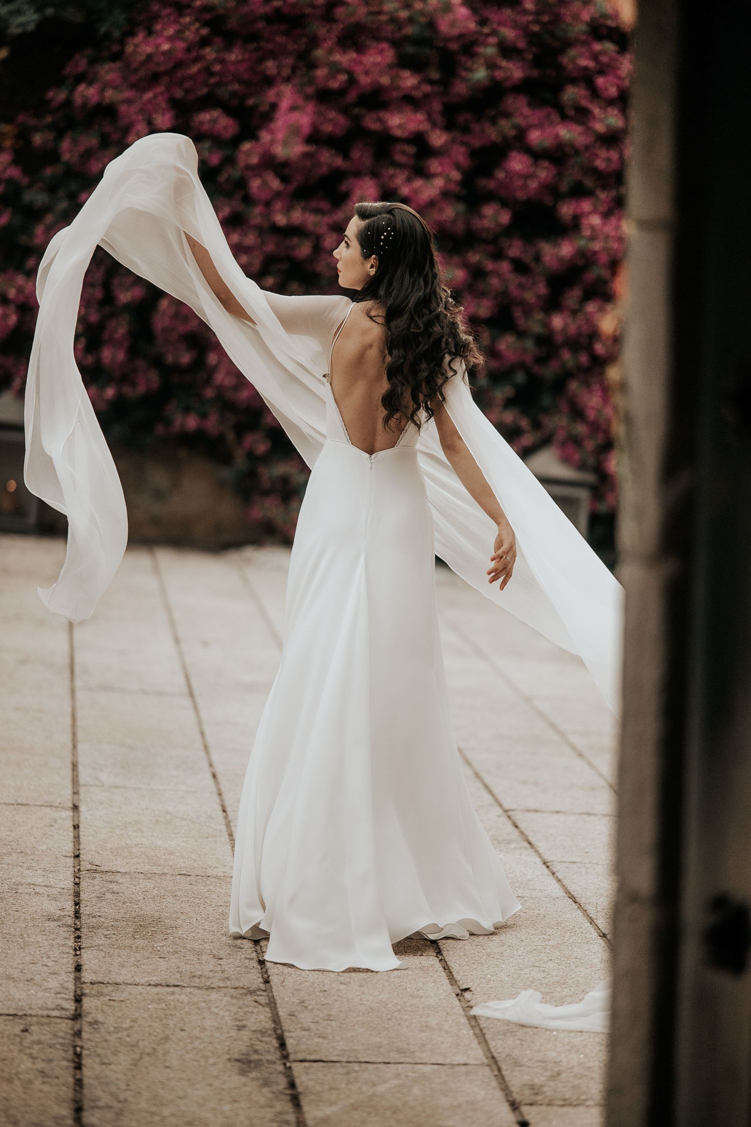A bride in a flowing white dress twirls gracefully against a backdrop of pink flowers.