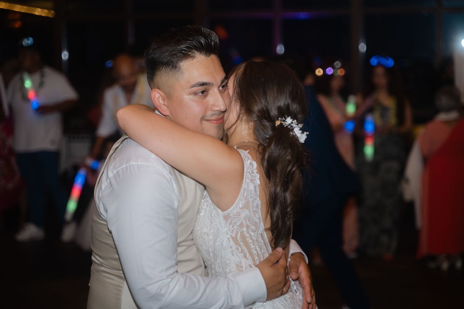 Couples dancing together at a dimly lit party venue with colorful lights in the background.