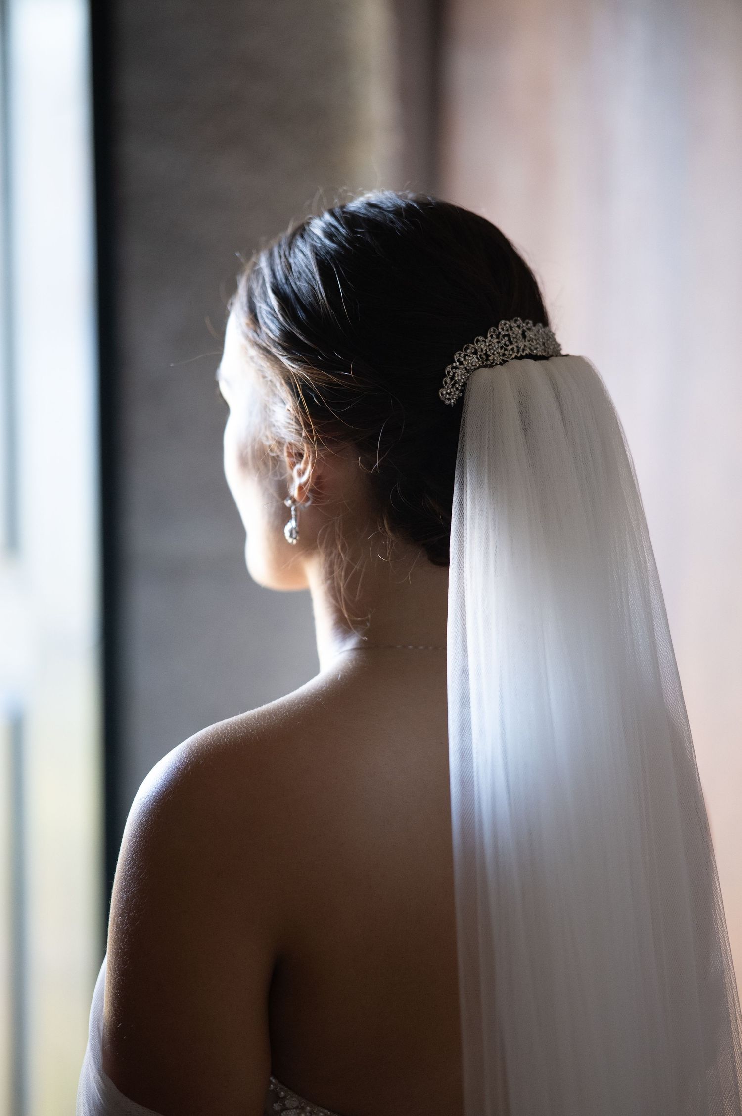A silhouetted bride wearing a veil stands in soft window light creating a dreamy bridal portrait.