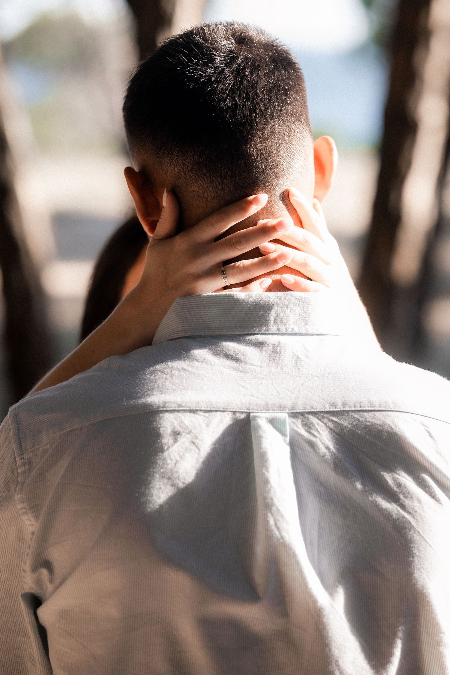 Back view of person in white shirt touching their neck in contemplative pose with blurred background.