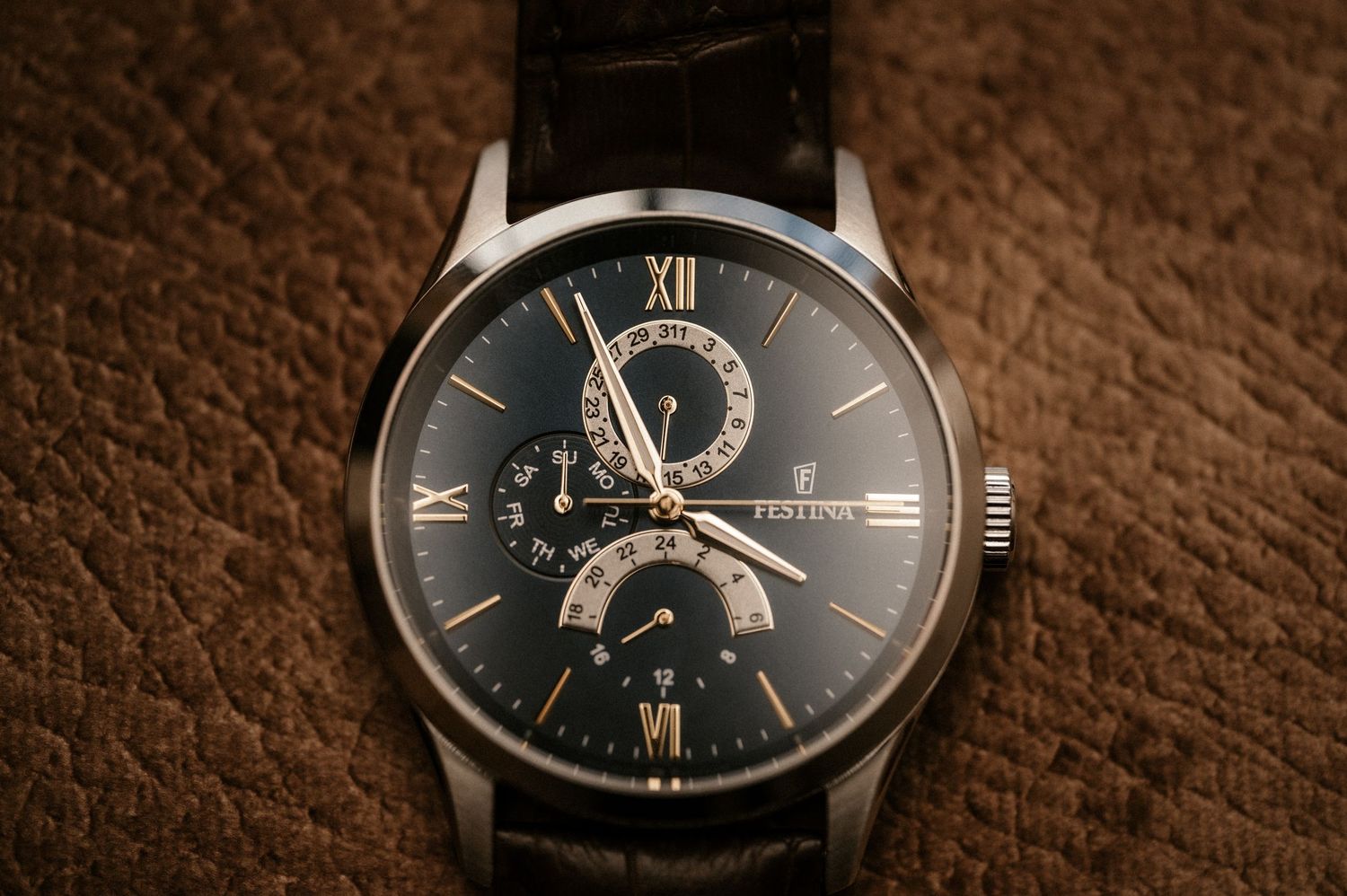 Luxury wristwatch with dark face and roman numerals displayed on textured brown leather surface.