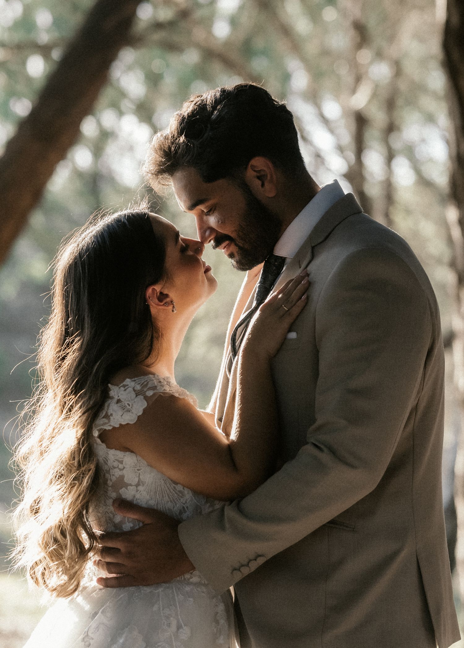 Romantic wedding couple sharing intimate moments in a sunlit forest setting.