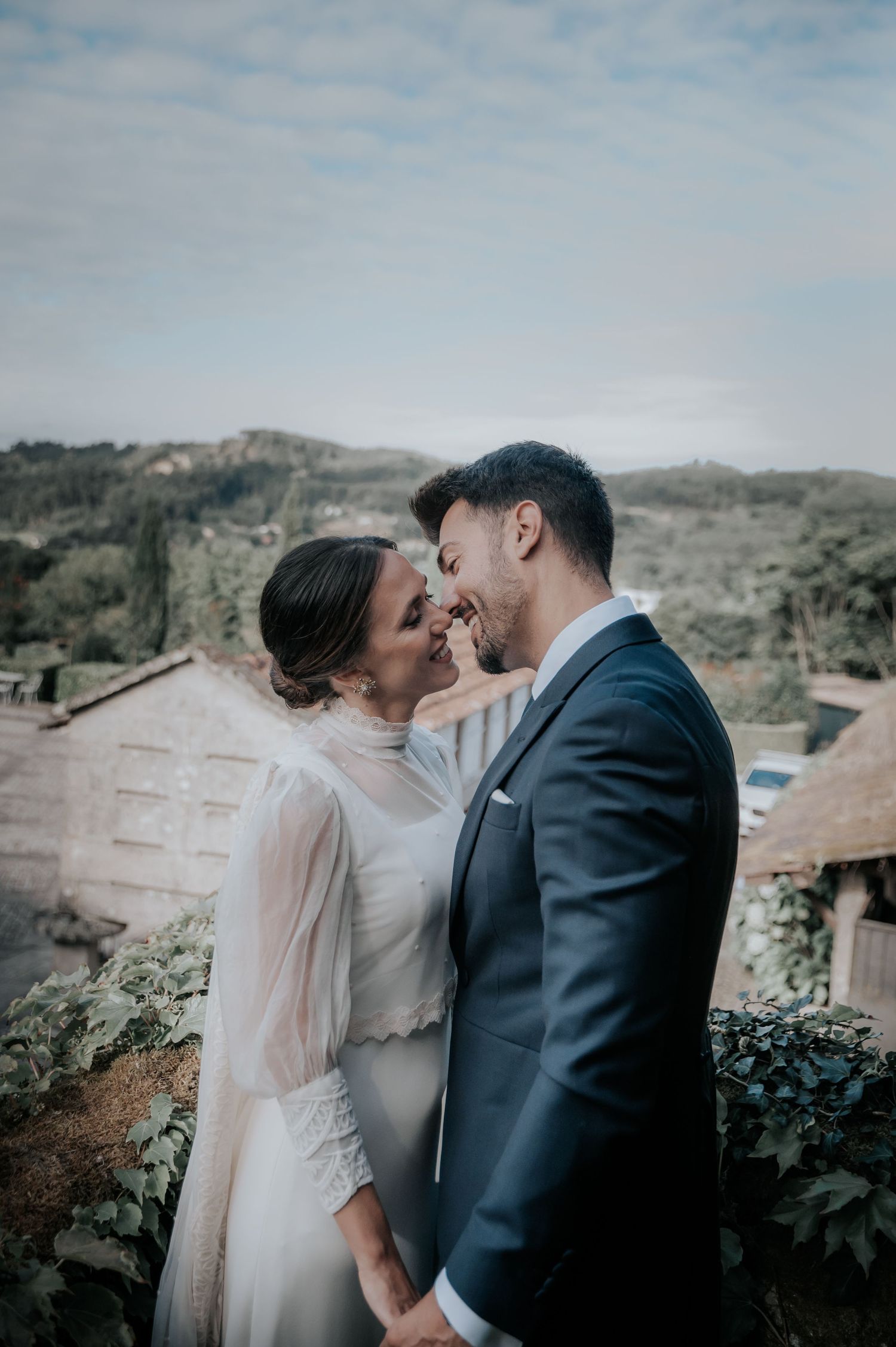 Romantic wedding couple sharing an intimate moment against a mountainous backdrop in soft lighting.
