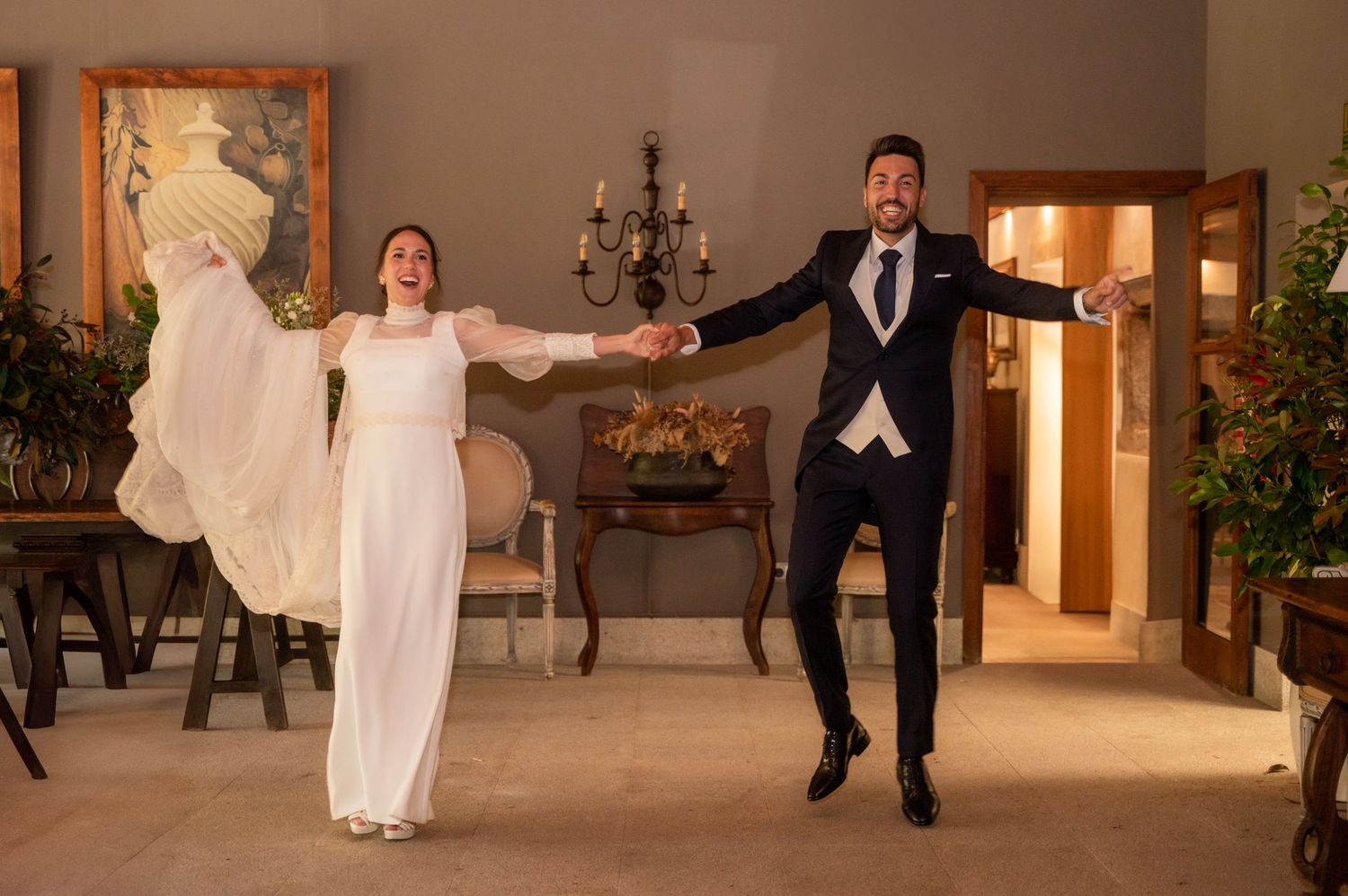 Wedding party members leap joyfully in formal attire against an elegant indoor venue backdrop.