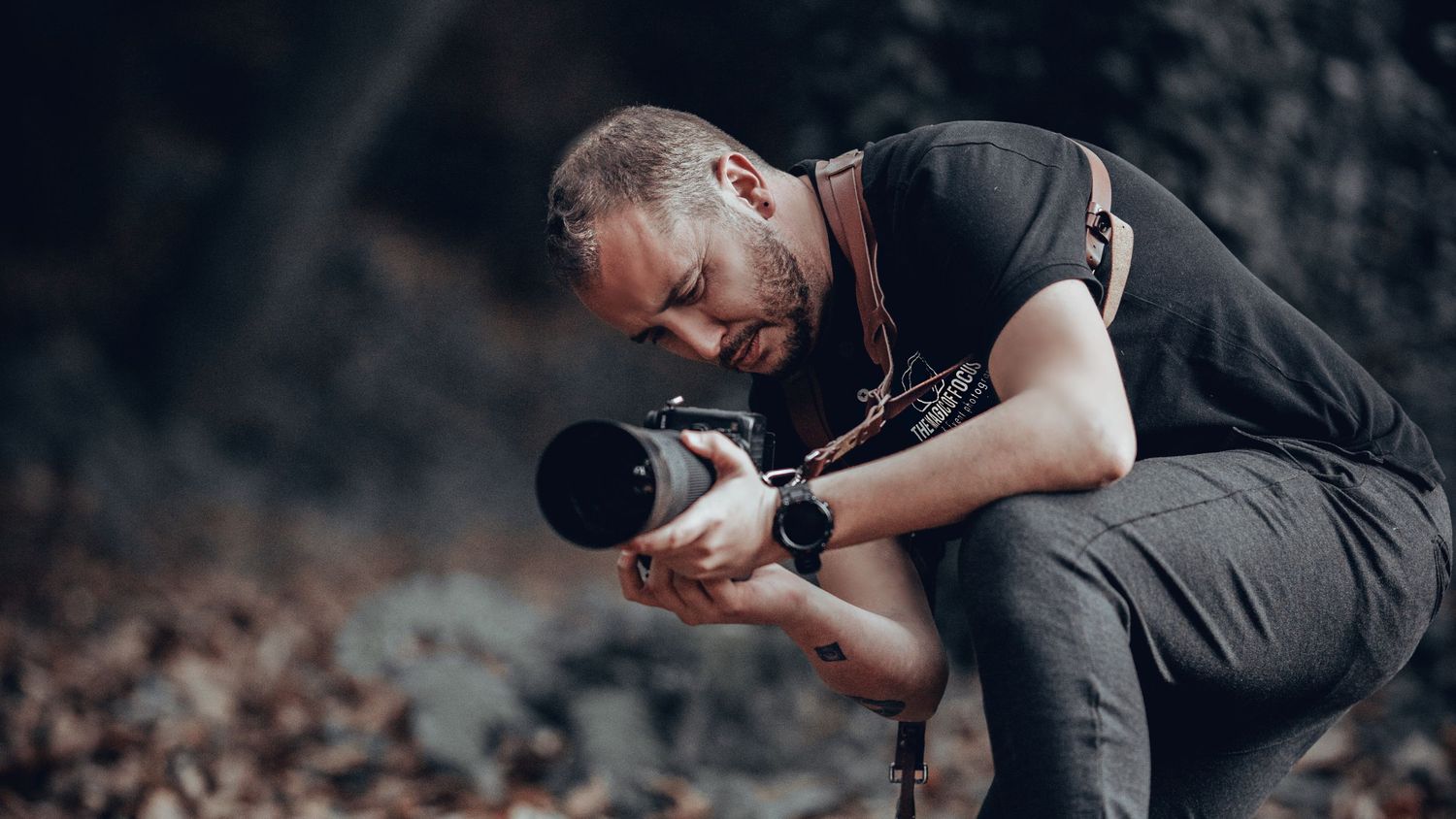 A photographer in dark clothing crouches down to capture a shot in a natural outdoor setting.