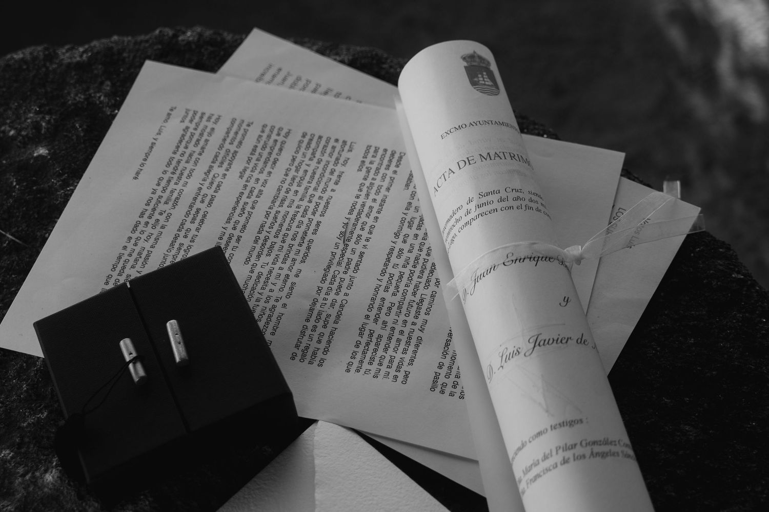 A black ring box sits beside rolled papers and documents in a black and white composition.