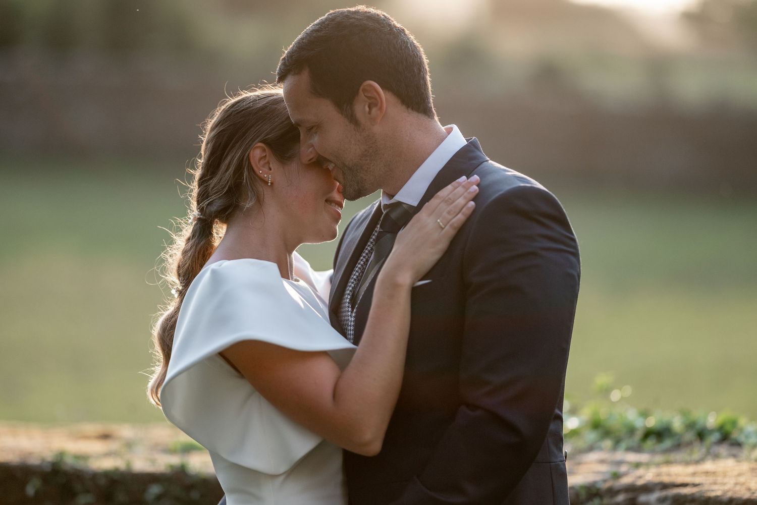 Romantic wedding couple embraces in golden sunlight during outdoor sunset photo session.