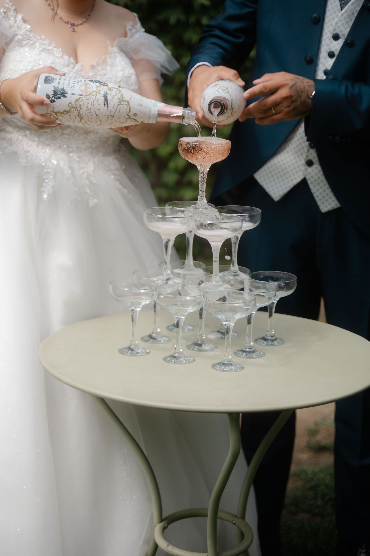 Champagne being poured into a tower of elegant crystal glasses arranged on a round white table at a wedding reception.