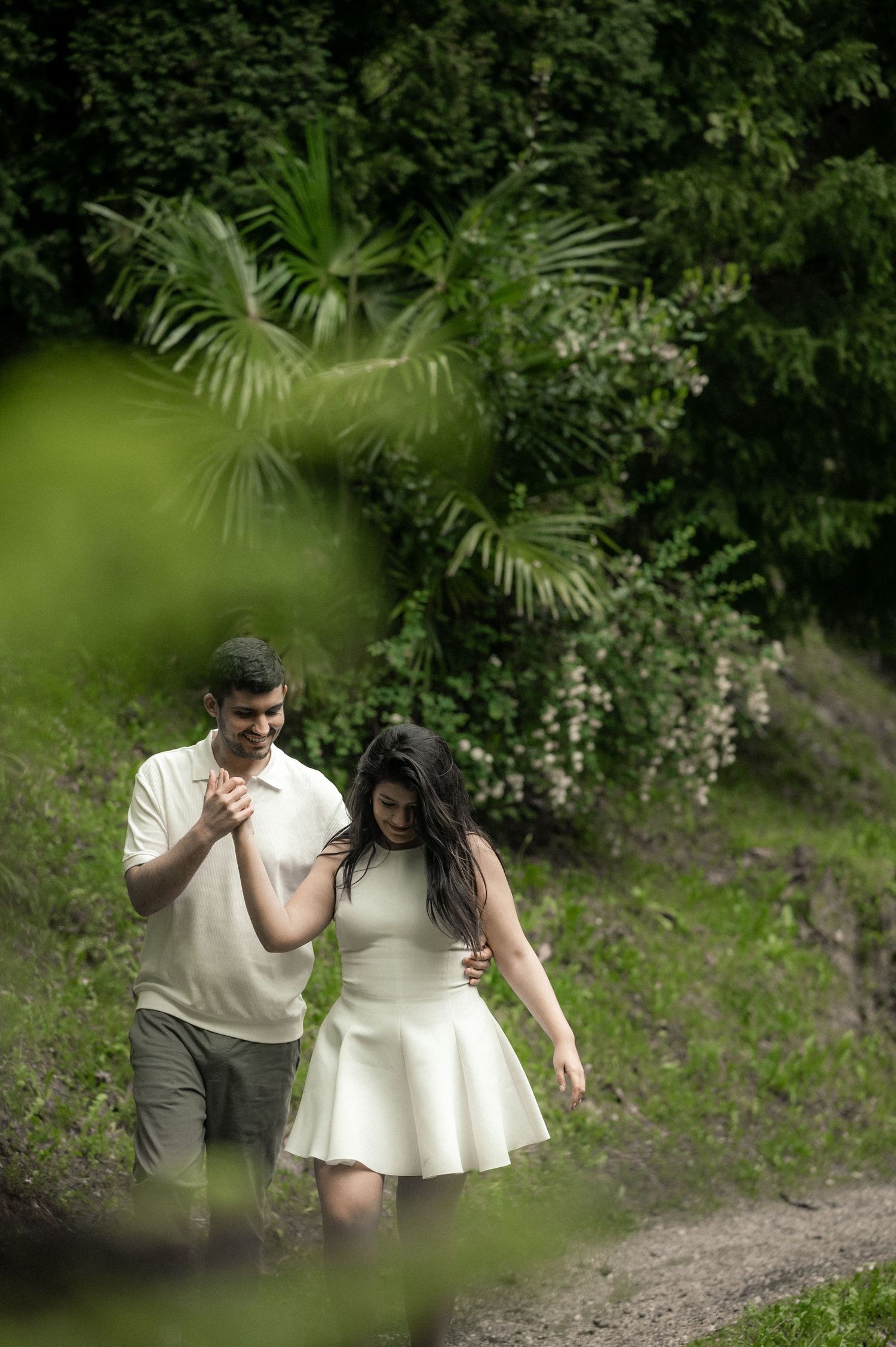 Couple in white and grey outfits share romantic moments in a lush tropical garden setting.