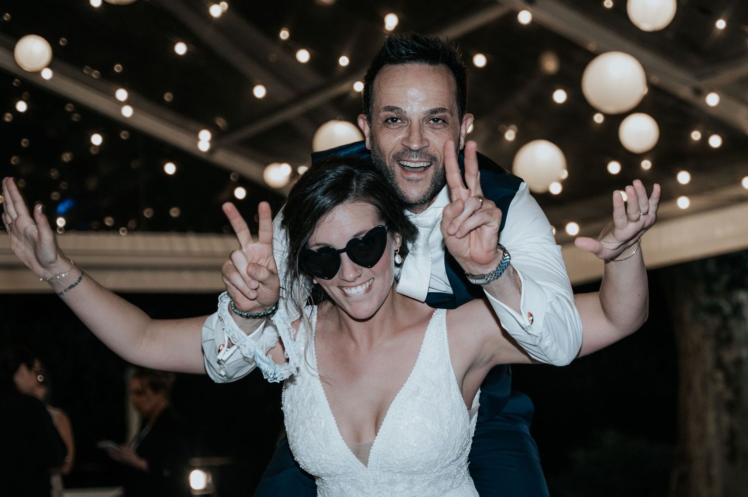 Wedding guests dance and celebrate under glowing white paper lanterns at an evening reception.