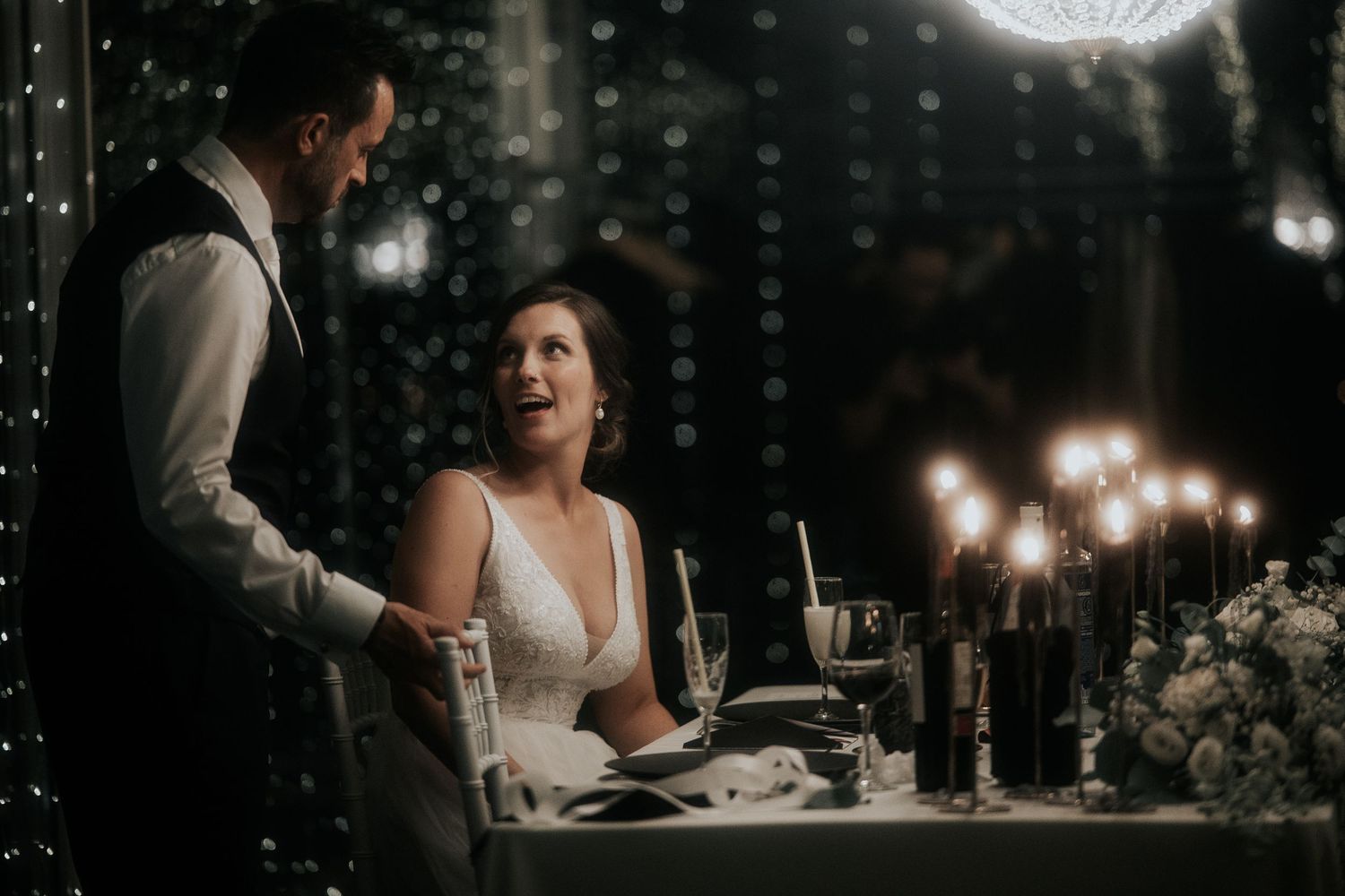 A romantic candlelit dinner scene at an elegant wedding reception with sparkly decor and mood lighting.