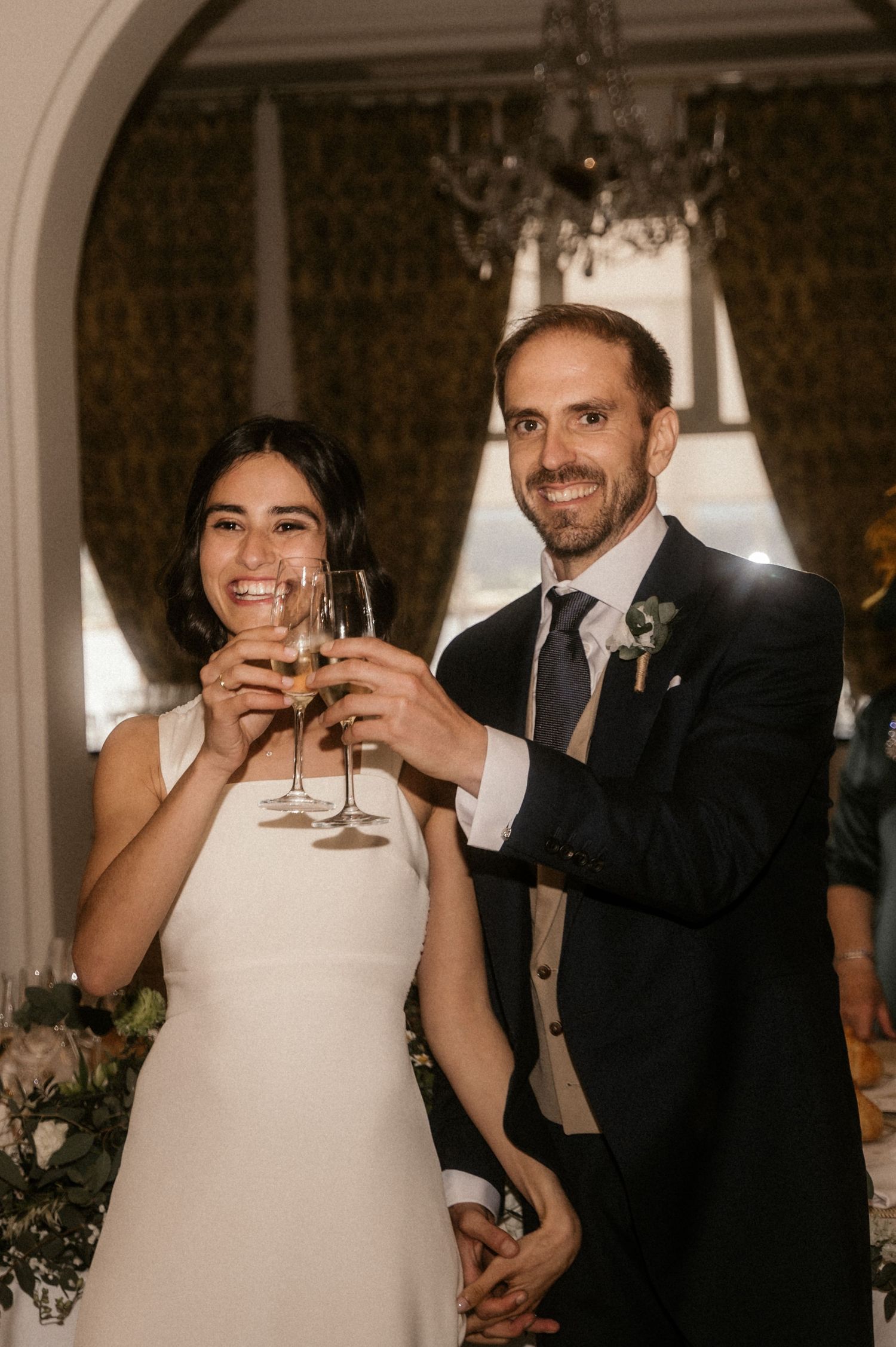 A couple in formal wedding attire toasts with wine glasses during their wedding celebration.