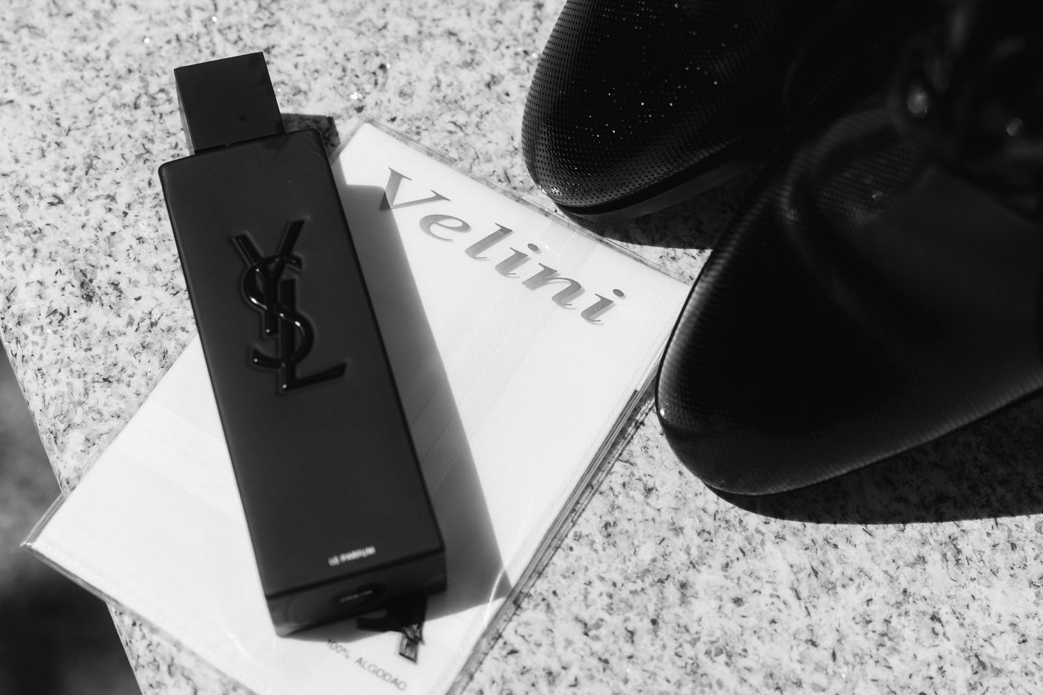 Monochrome fashion flatlay featuring luxury designer items including black accessories and boxes on a marble surface.