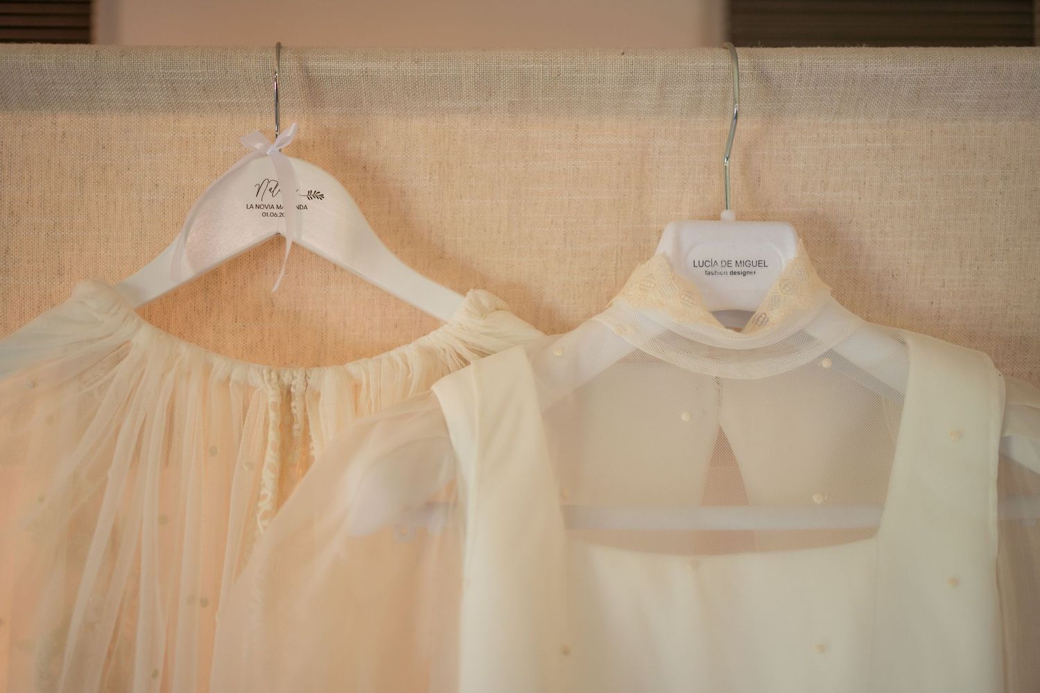 A collection of delicate white and cream colored vintage dresses hanging on wooden hangers against a light background.