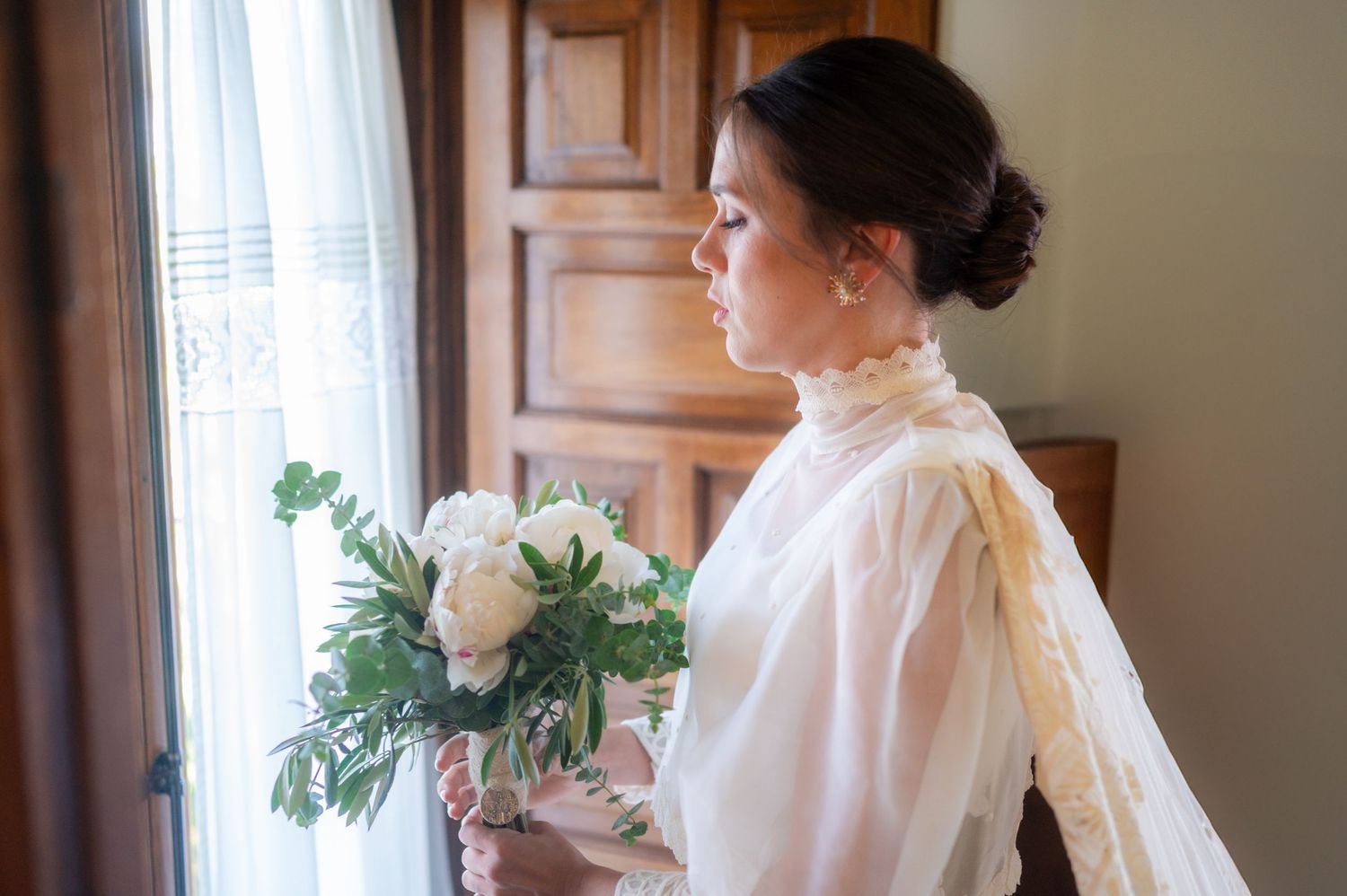 Elegant bridal preparation scene with flowing white robe and veil near sunlit window.