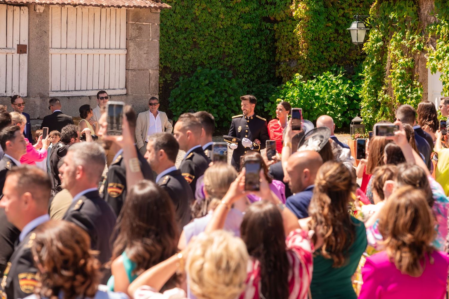 A crowd of people outdoors holding up phones and cameras to capture a moment at a sunny gathering.